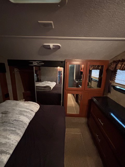 Functional RV rental bedroom interior with a bed, mirrored wardrobe, and dresser, ideal for travel stays.. Keystone RV Fuzion Toy Hauler 2009