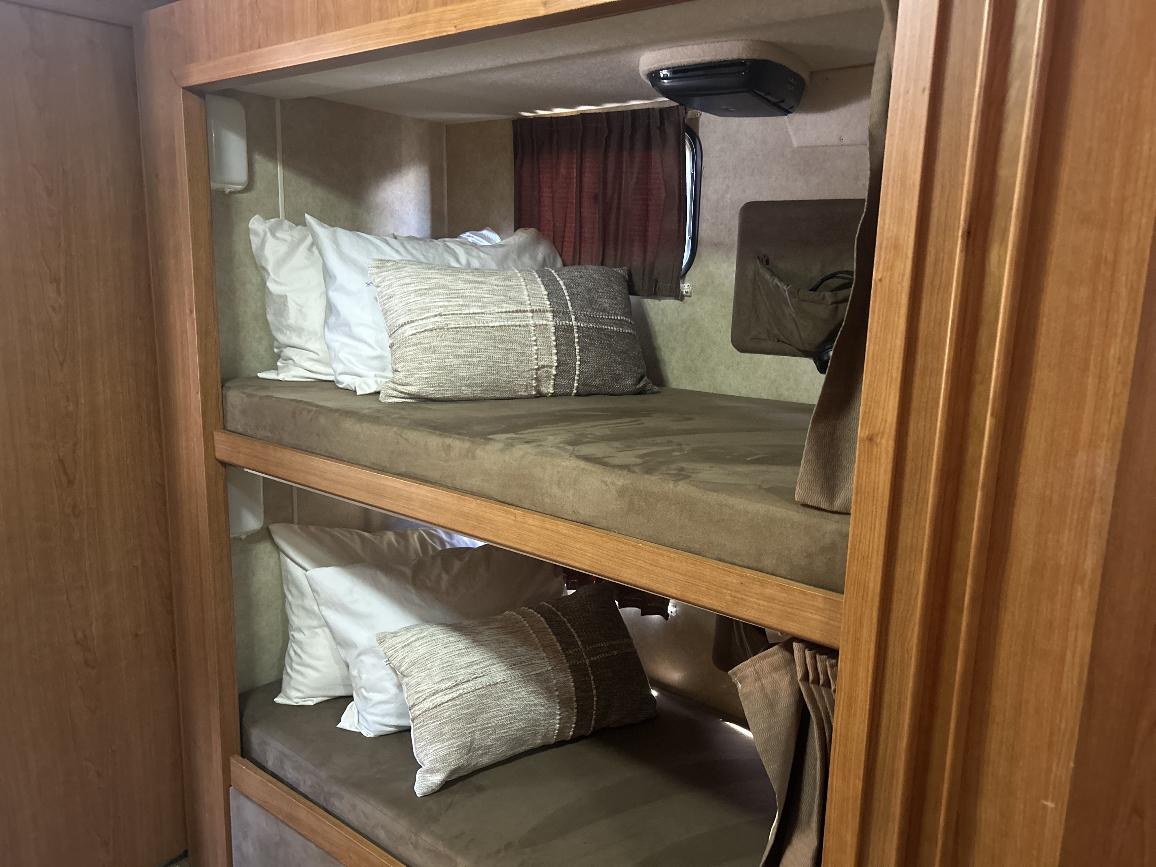 Cozy RV rental bunk beds with brown cushions and various pillows for comfortable sleeping. Ideal for family adventures.. Winnebago Sightseer 2009