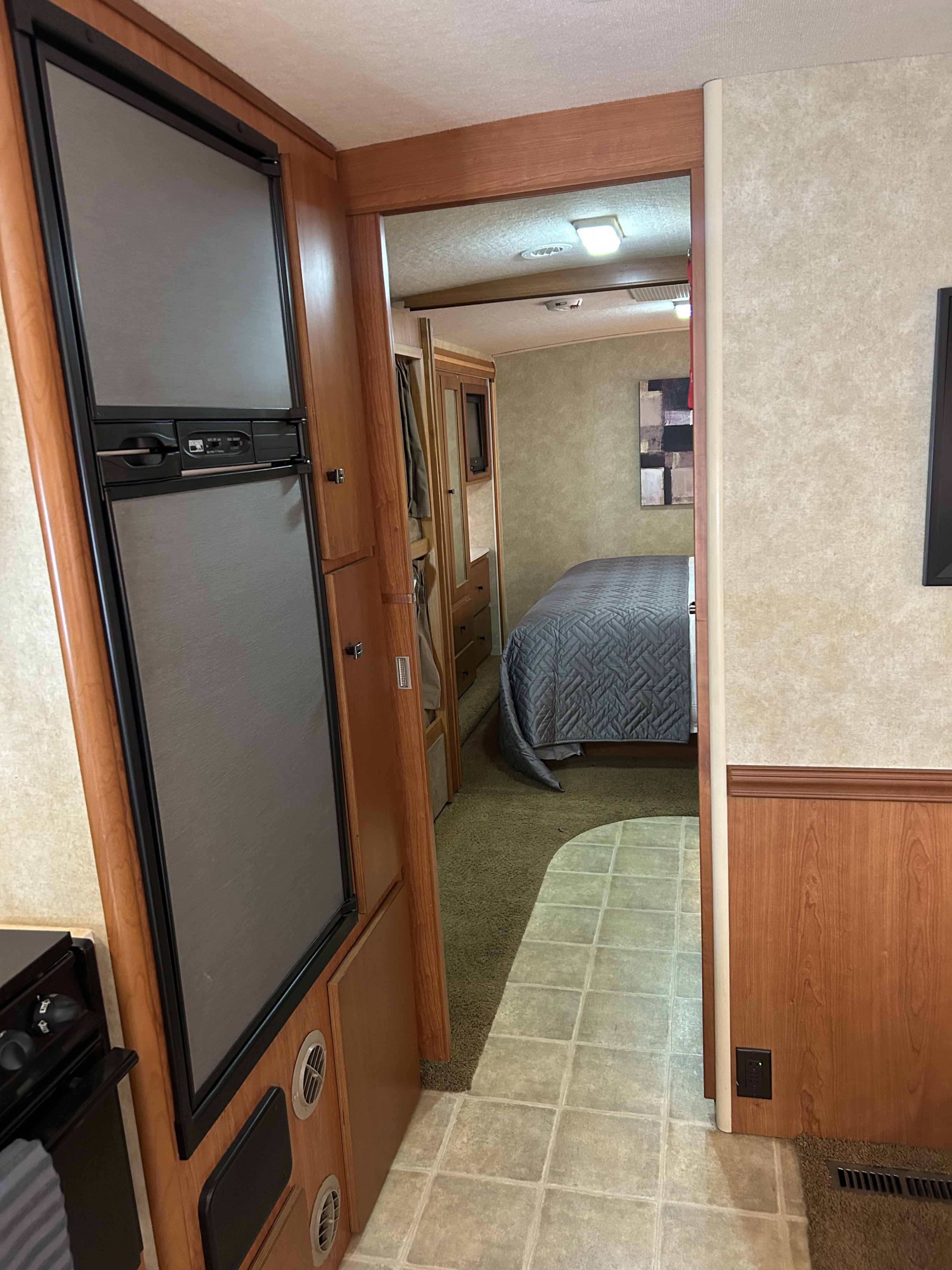 Cozy rv rental interior: bedroom with quilted bed visible through hallway. Built-in fridge in foreground, tile to carpet transition.. Winnebago Sightseer 2009