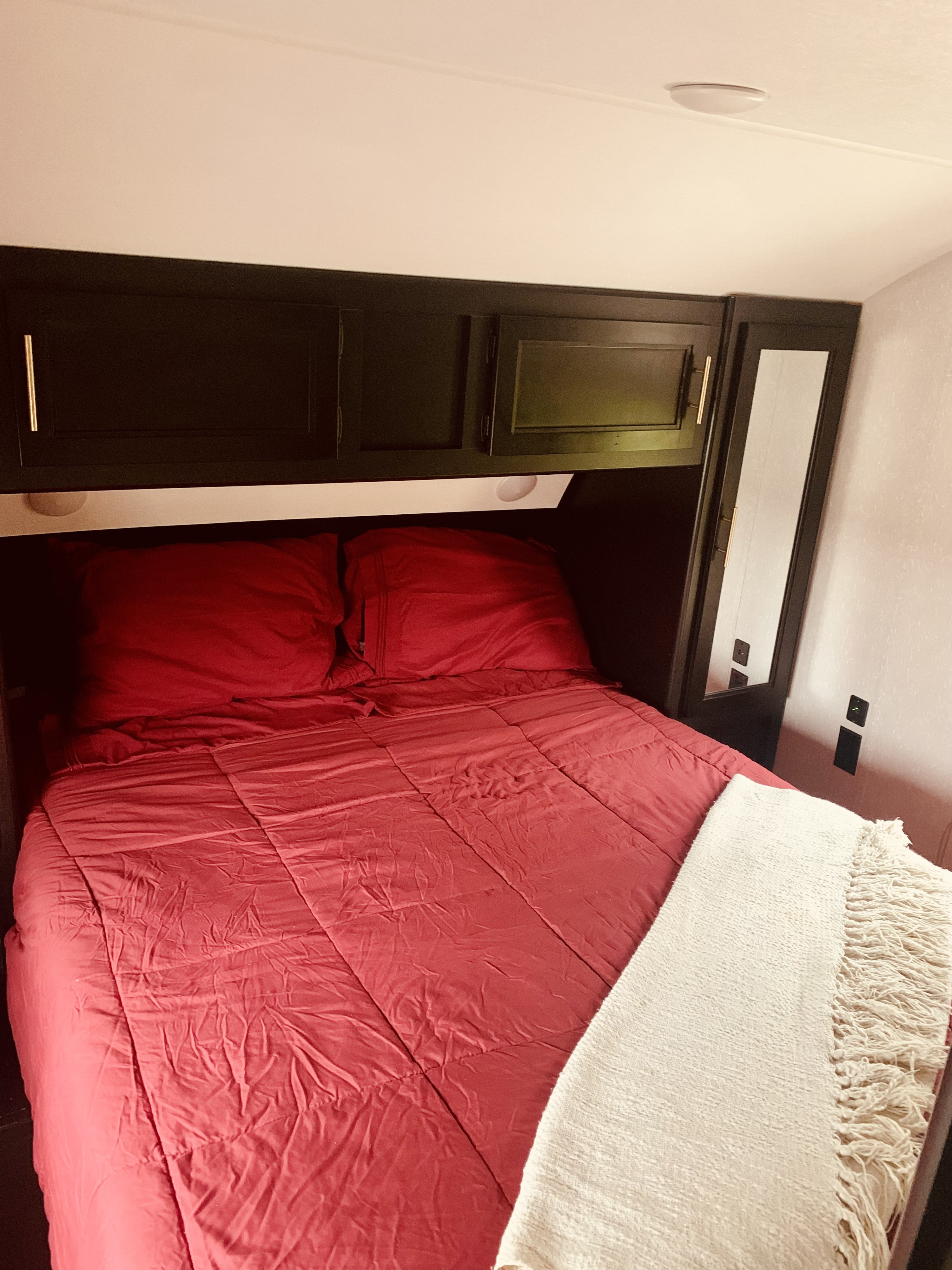 Cozy RV rental bedroom featuring a bed with red bedding, dark overhead storage, and a mirrored wardrobe, ideal for travel.. Forest River Cherokee Grey Wolf 2021