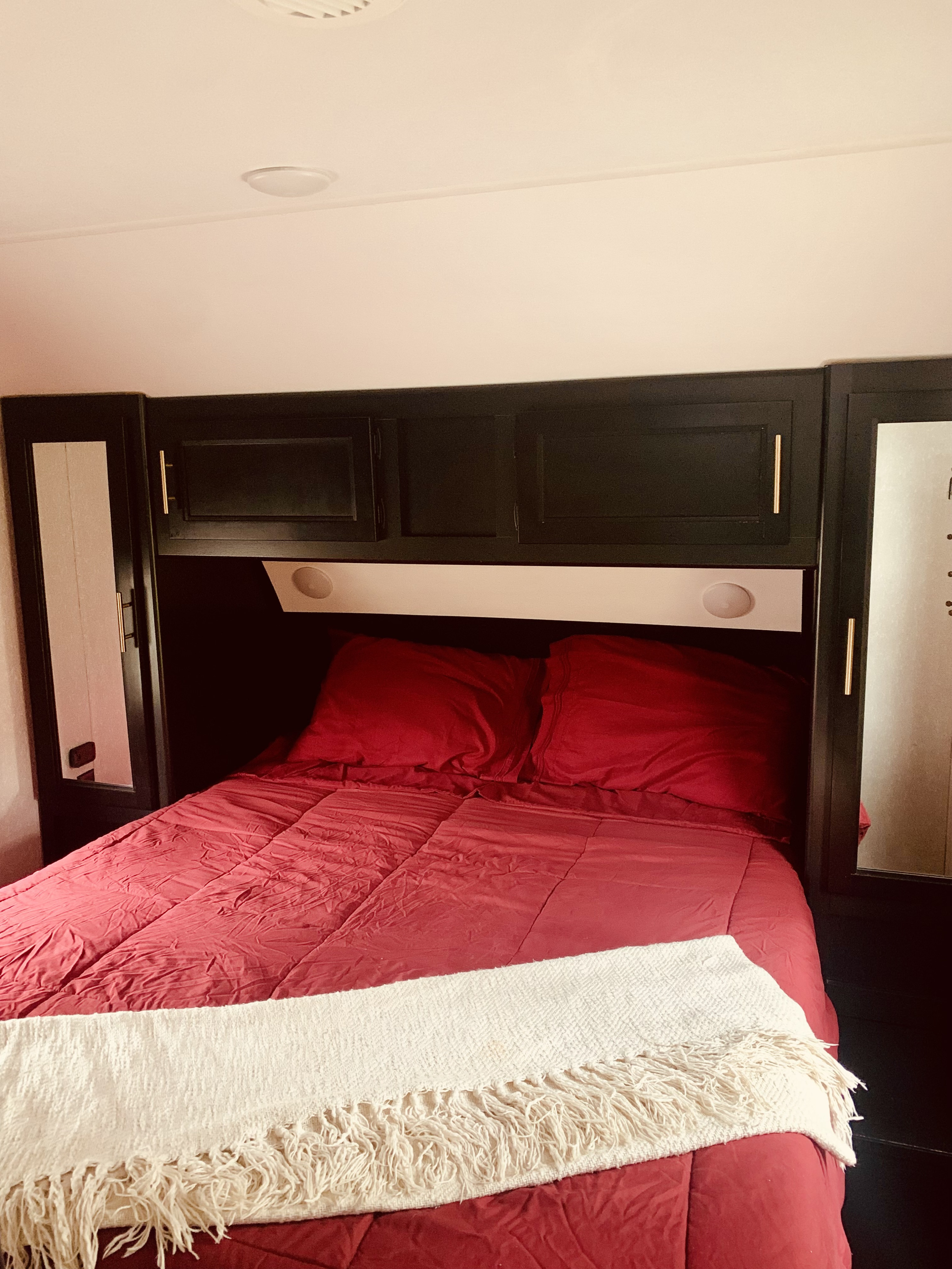 Cozy RV rental bedroom featuring a bed with red bedding, a white throw, and built-in dark cabinetry.. Forest River Cherokee Grey Wolf 2021