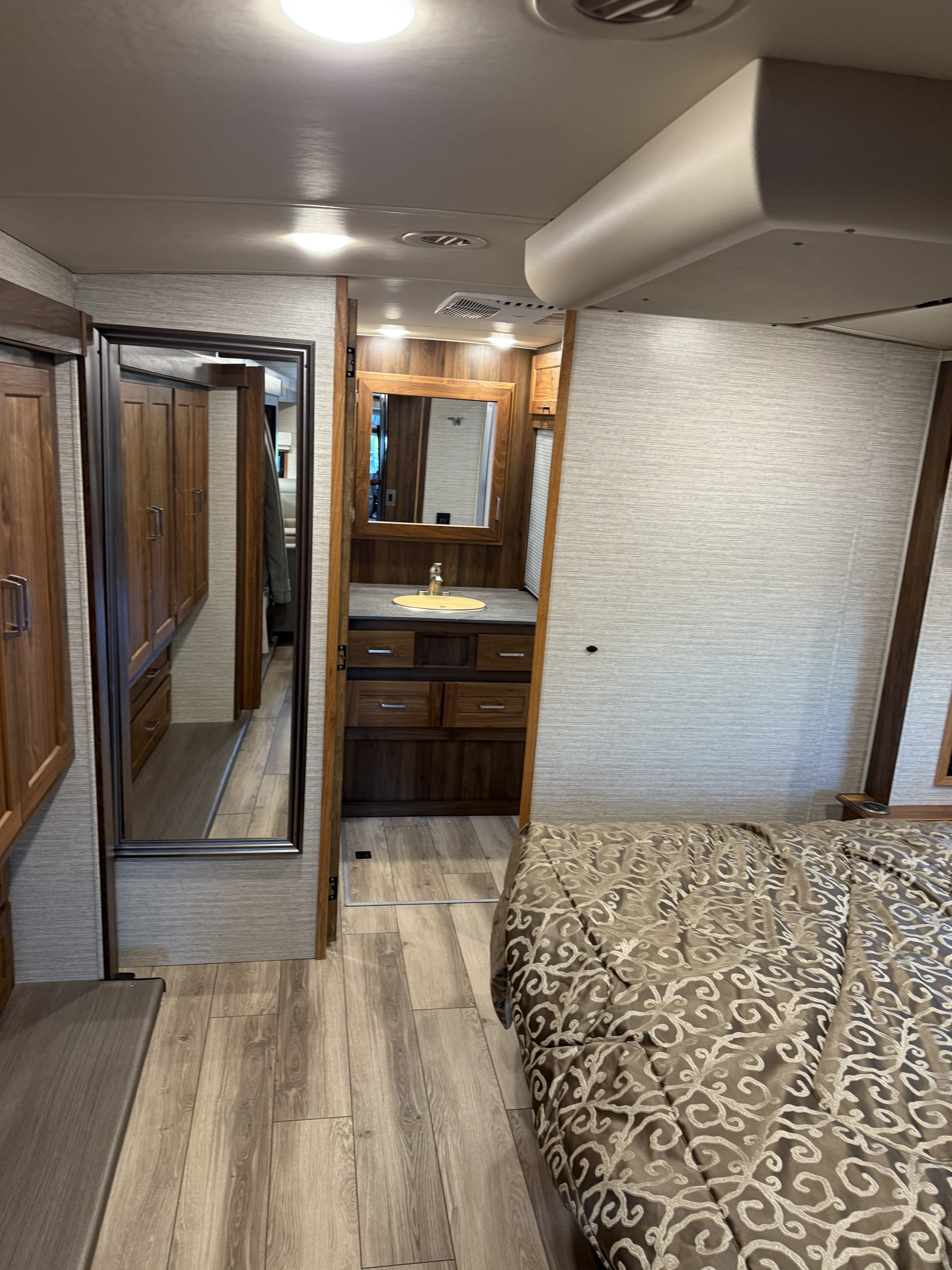 RV rental interior featuring a bedroom with a patterned bed and a view into a bathroom vanity with sink and mirror.. Winnebago Forza 2021