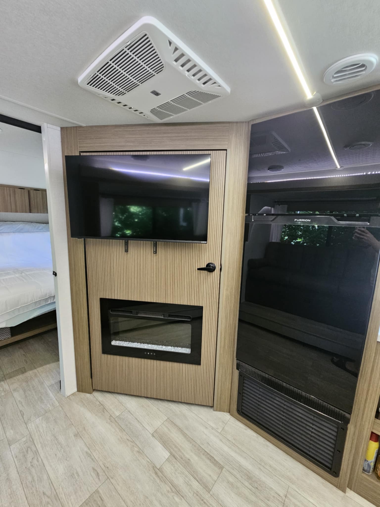 Interior of an RV rental: features a wall-mounted TV, electric fireplace, large refrigerator, and a light-filled bedroom. Modern design.. Forest River 26Ice 2025