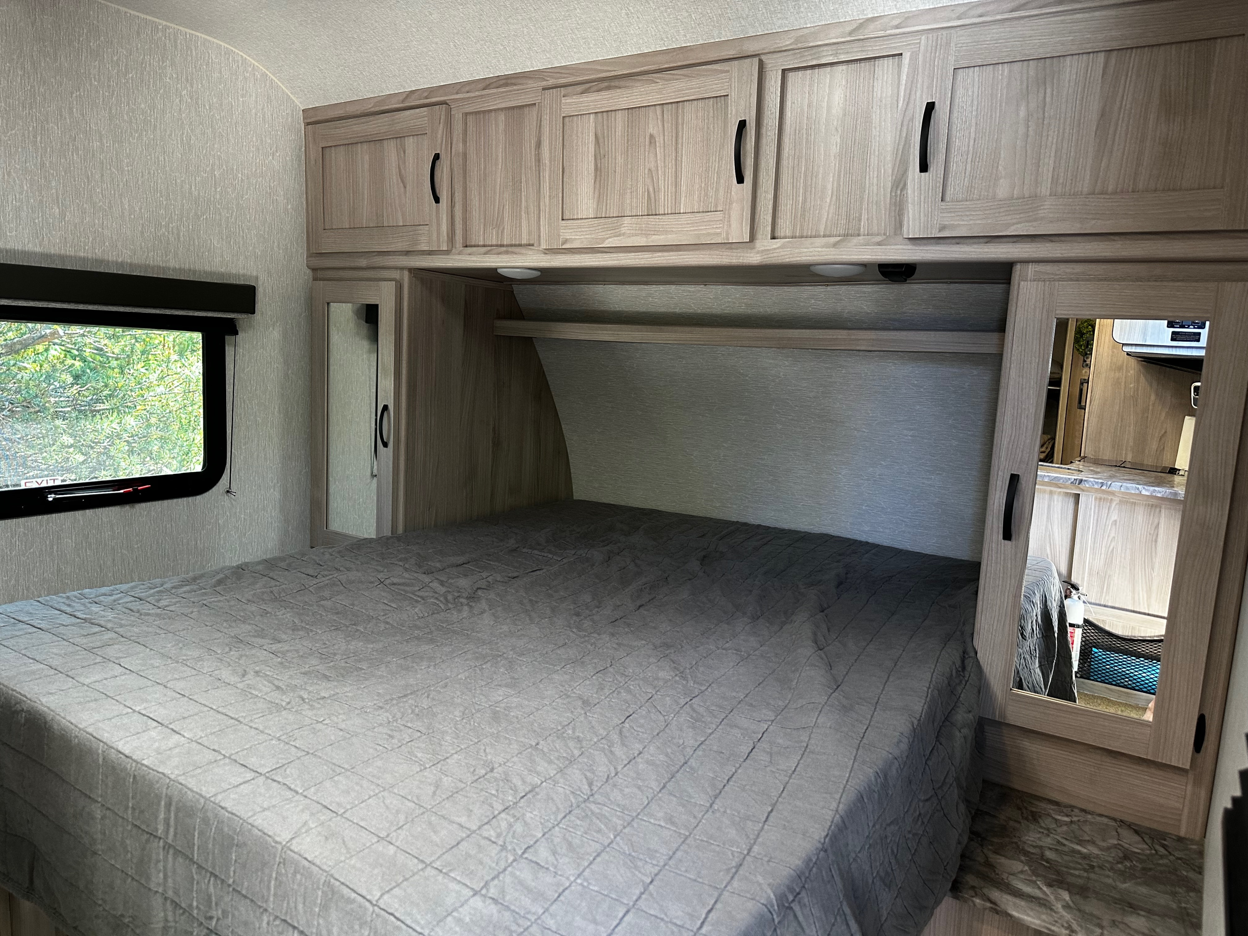 RV rental bedroom interior with a gray bed, light wood cabinets, window, and mirrored closet door.. Coachmen Spirit SBT2963BH 2022
