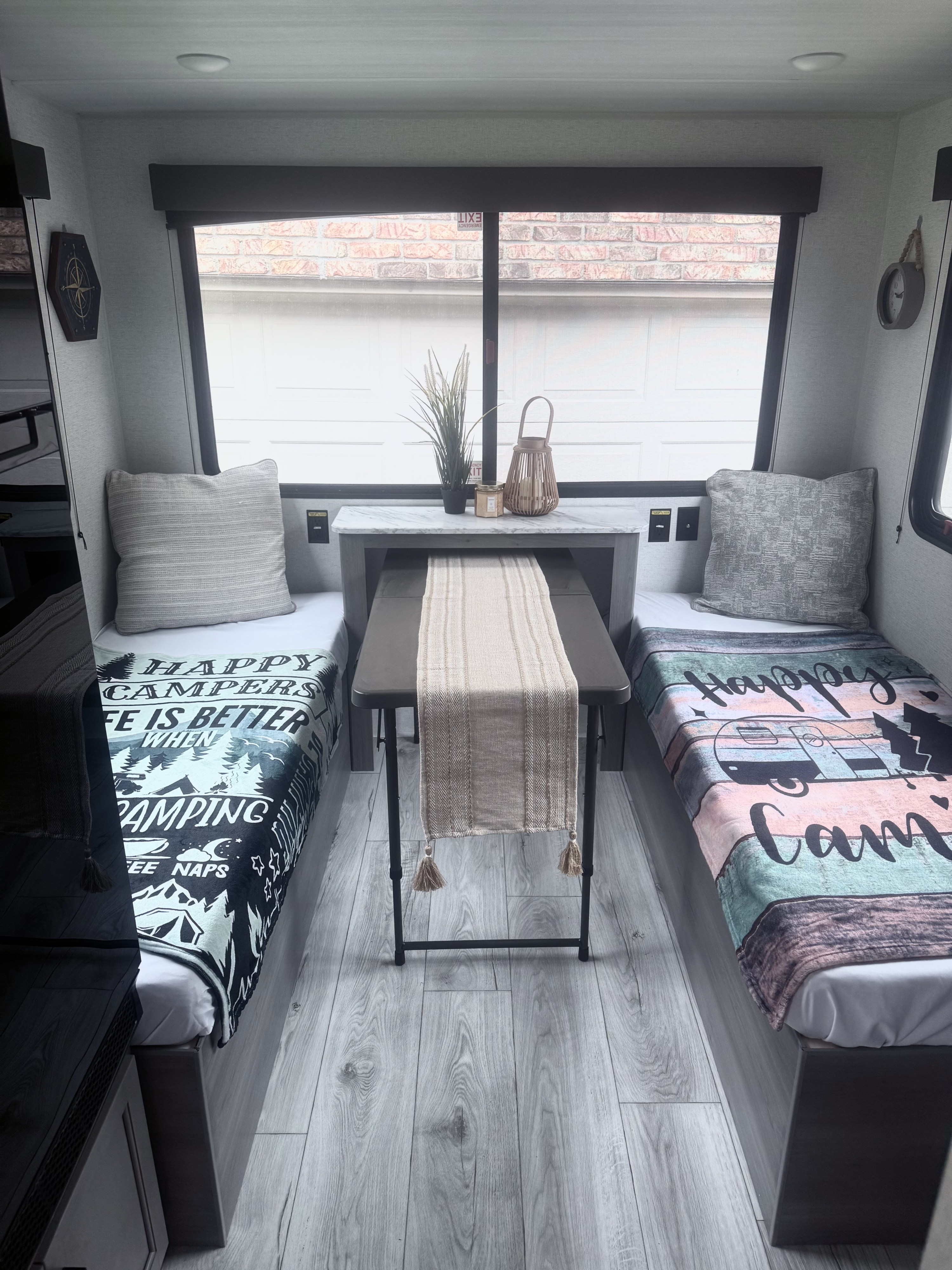 Cozy RV rental interior featuring twin beds with camping blankets, a central dining table, and homey decor.. Keystone HIDEOUT 2025