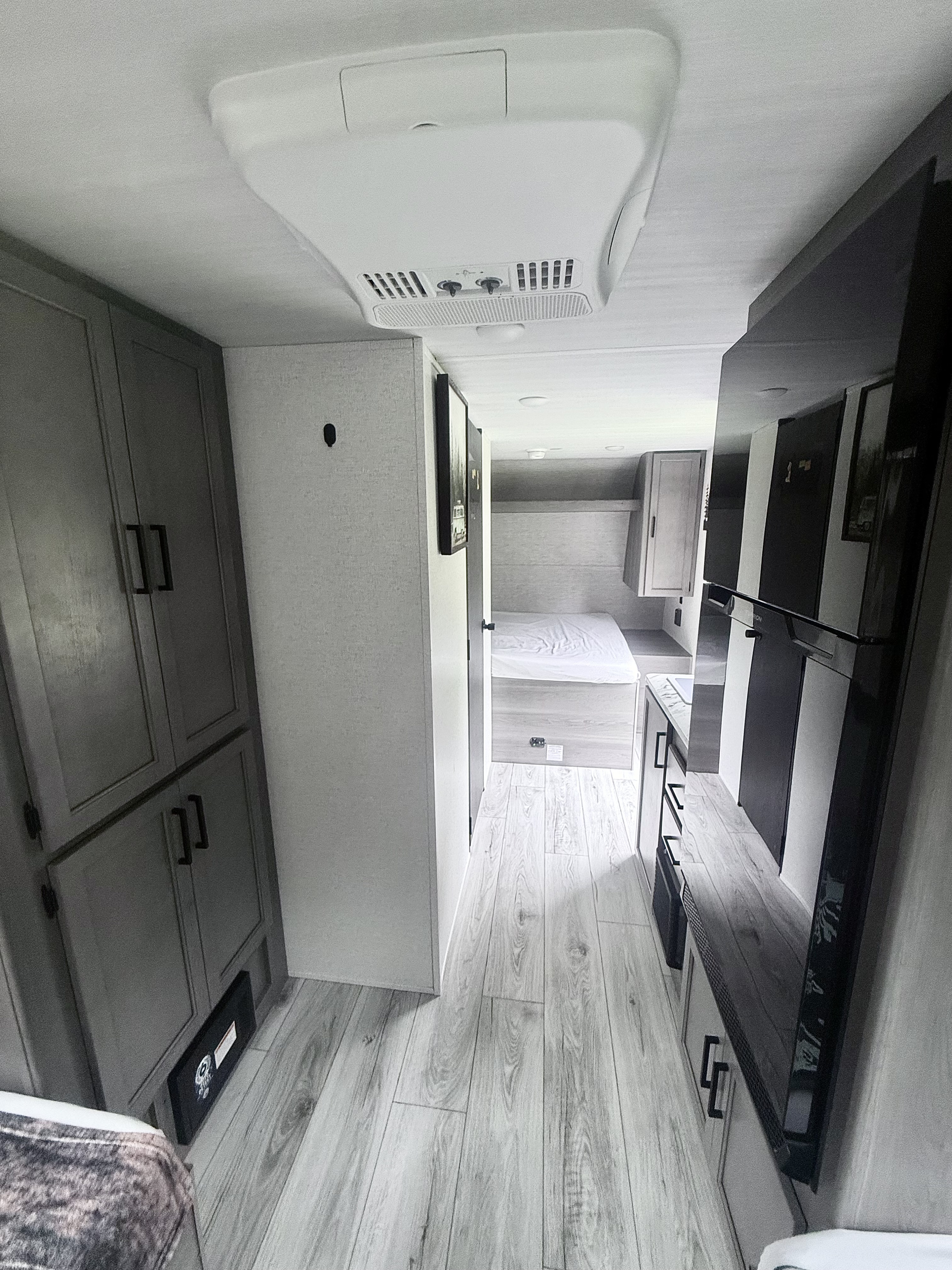 Spacious RV rental interior: modern design with wood-look floors, grey cabinets, leading to kitchen and bedroom.. Keystone HIDEOUT 2025