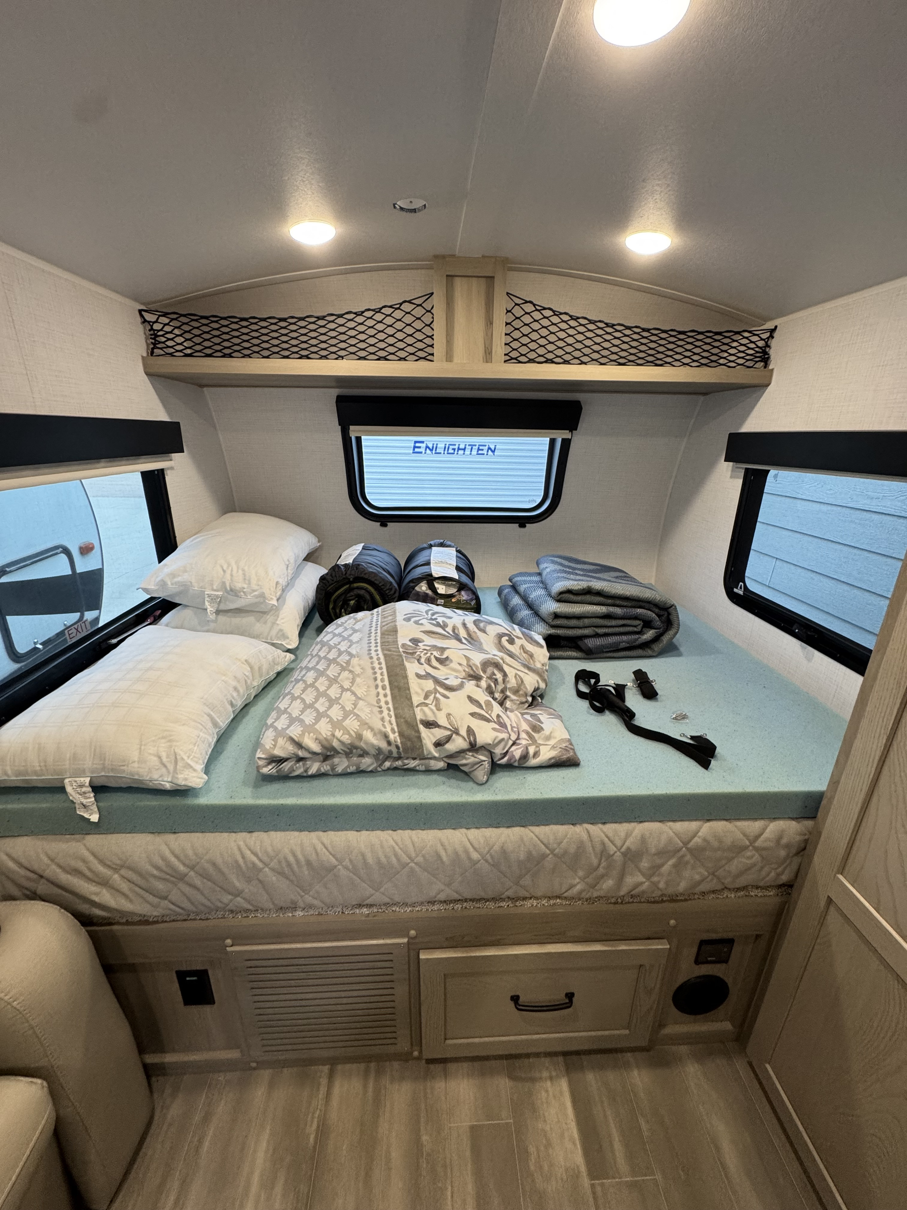 An RV rental bedroom featuring a comfy bed with blue topper, pillows, blankets, and handy overhead storage nets.. Forest River Rockwood Geo Pro 2024