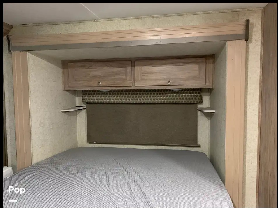 RV rental interior: cozy bedroom with bed, overhead cabinets, and a window with a pulled shade.. Forest River Sunseeker LE 2020