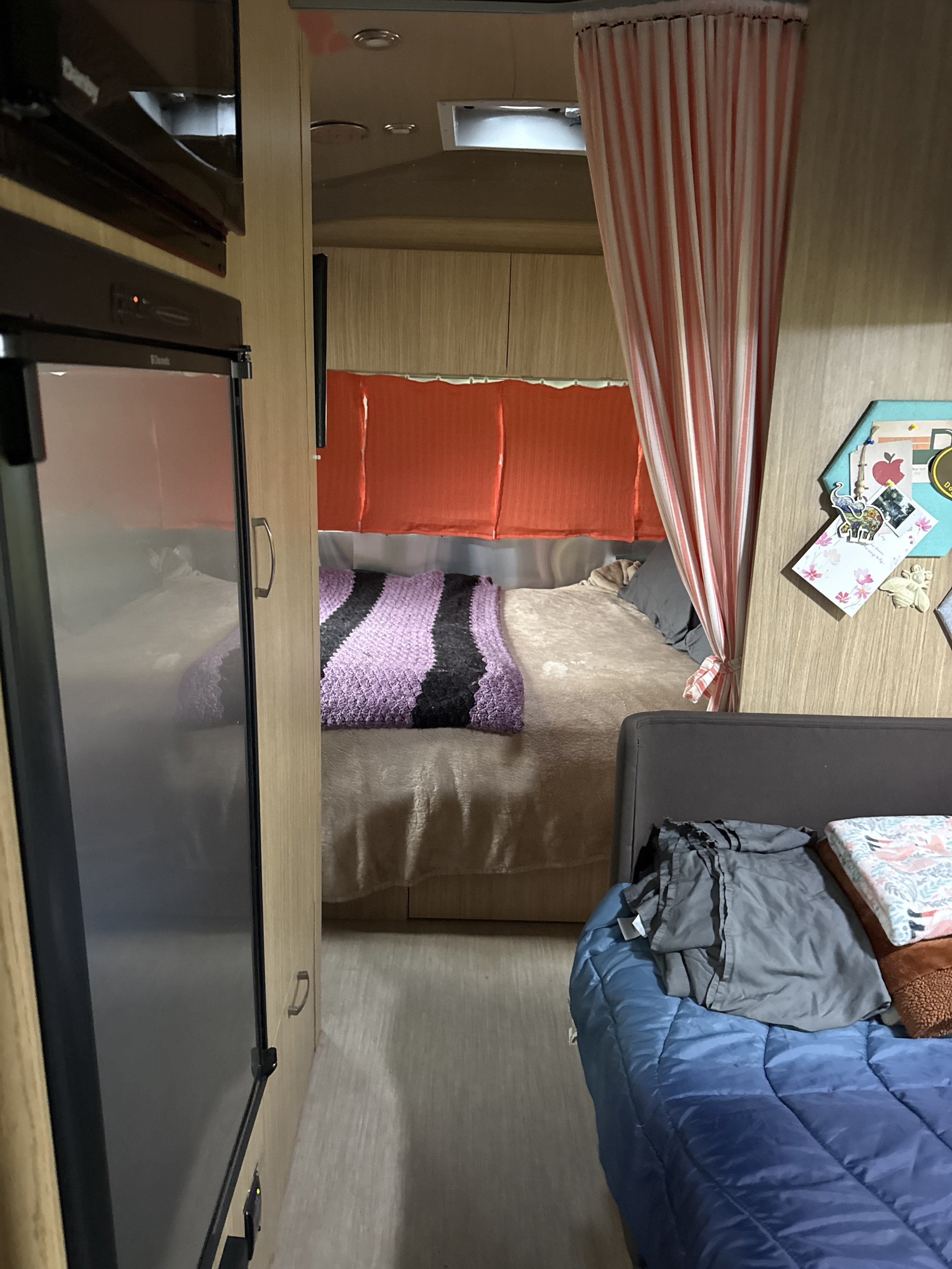 Spacious RV rental interior: fridge on left, main bed with purple blanket & orange blinds, and second sleeping area on right.. Airstream Flying Cloud 2018
