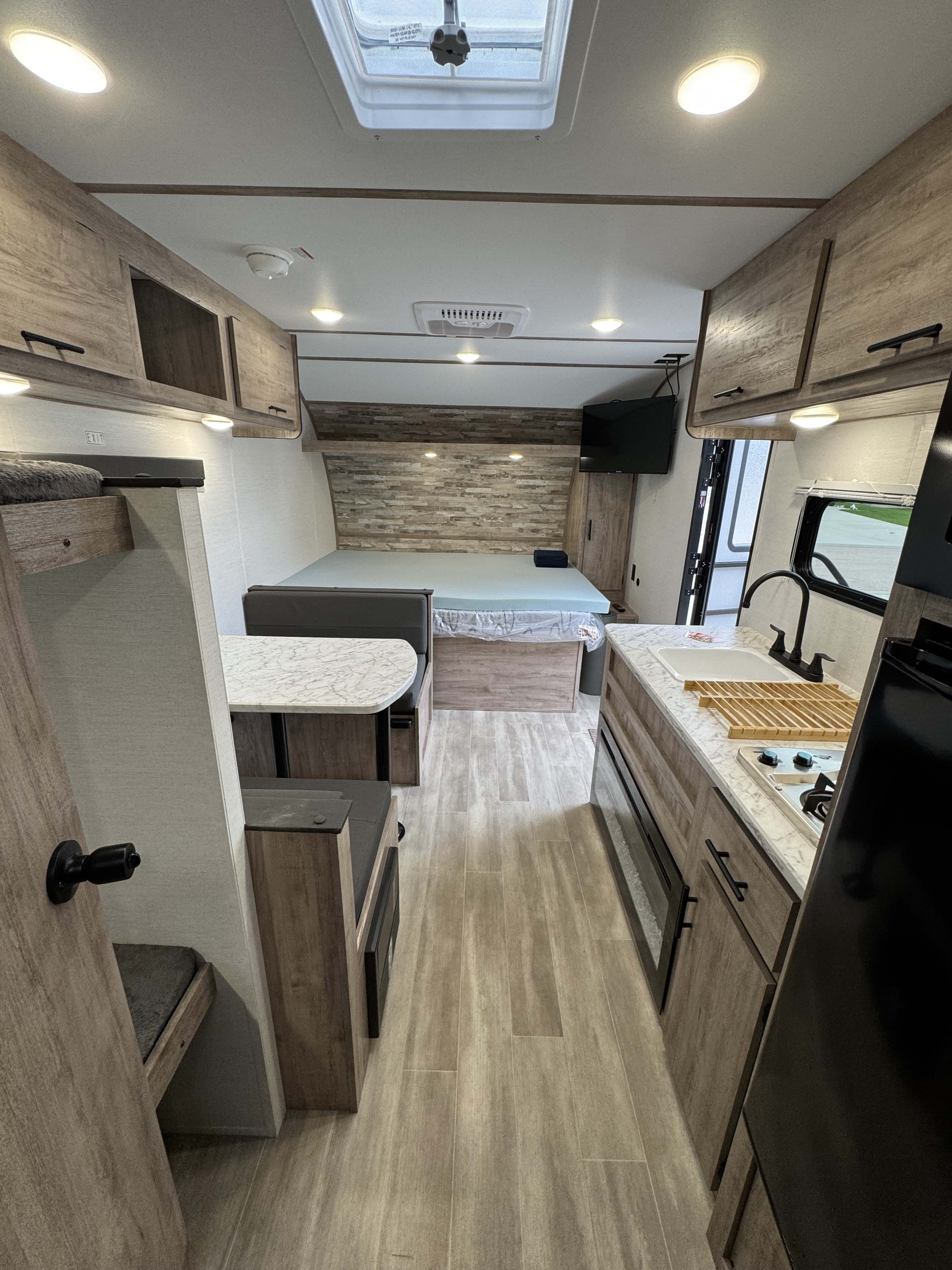 Modern RV rental interior with kitchen, dinette, and cozy bed. Features include overhead storage & wood-look flooring.. Gulf Stream Coach Enlighten 17bh 2025