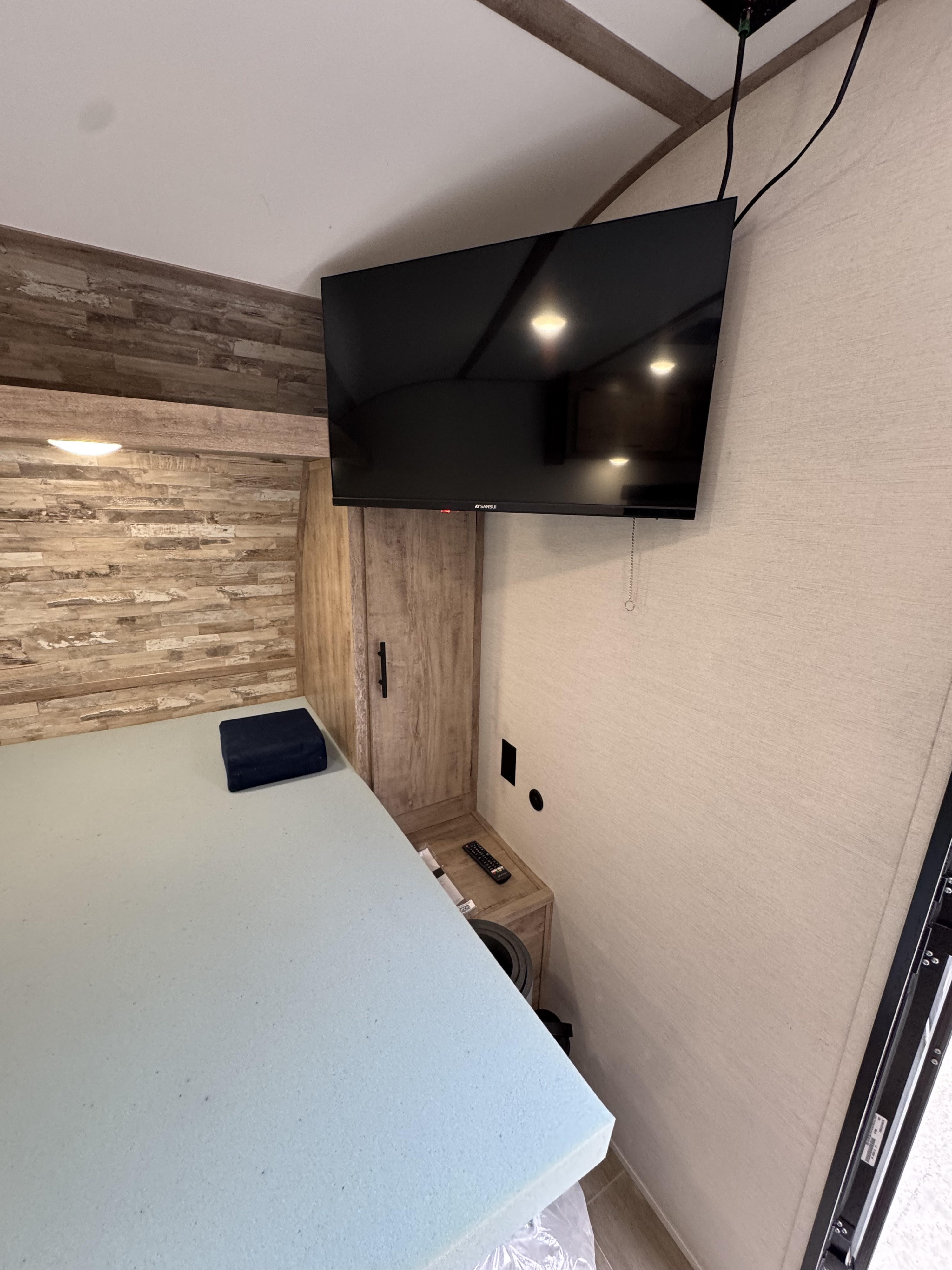 Inside an RV rental: a compact bedroom features a light blue mattress, wall-mounted TV, and wooden cabinet storage.. Gulf Stream Coach Enlighten 17bh 2025