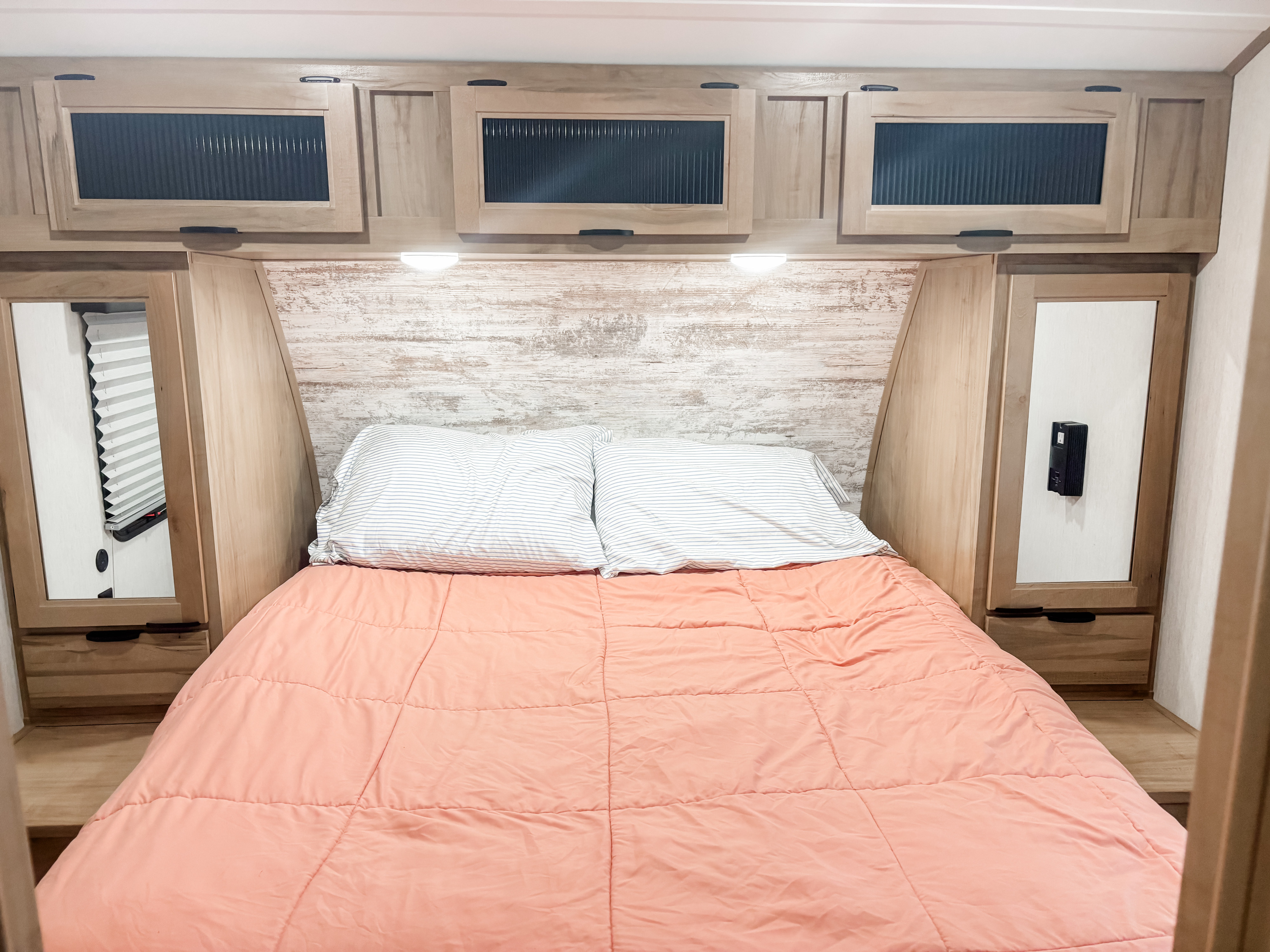 Cozy RV rental bedroom featuring a bed with pink comforter, striped pillows, light wood cabinets & mirrored wardrobes.. Forest River 33BH-L 2024