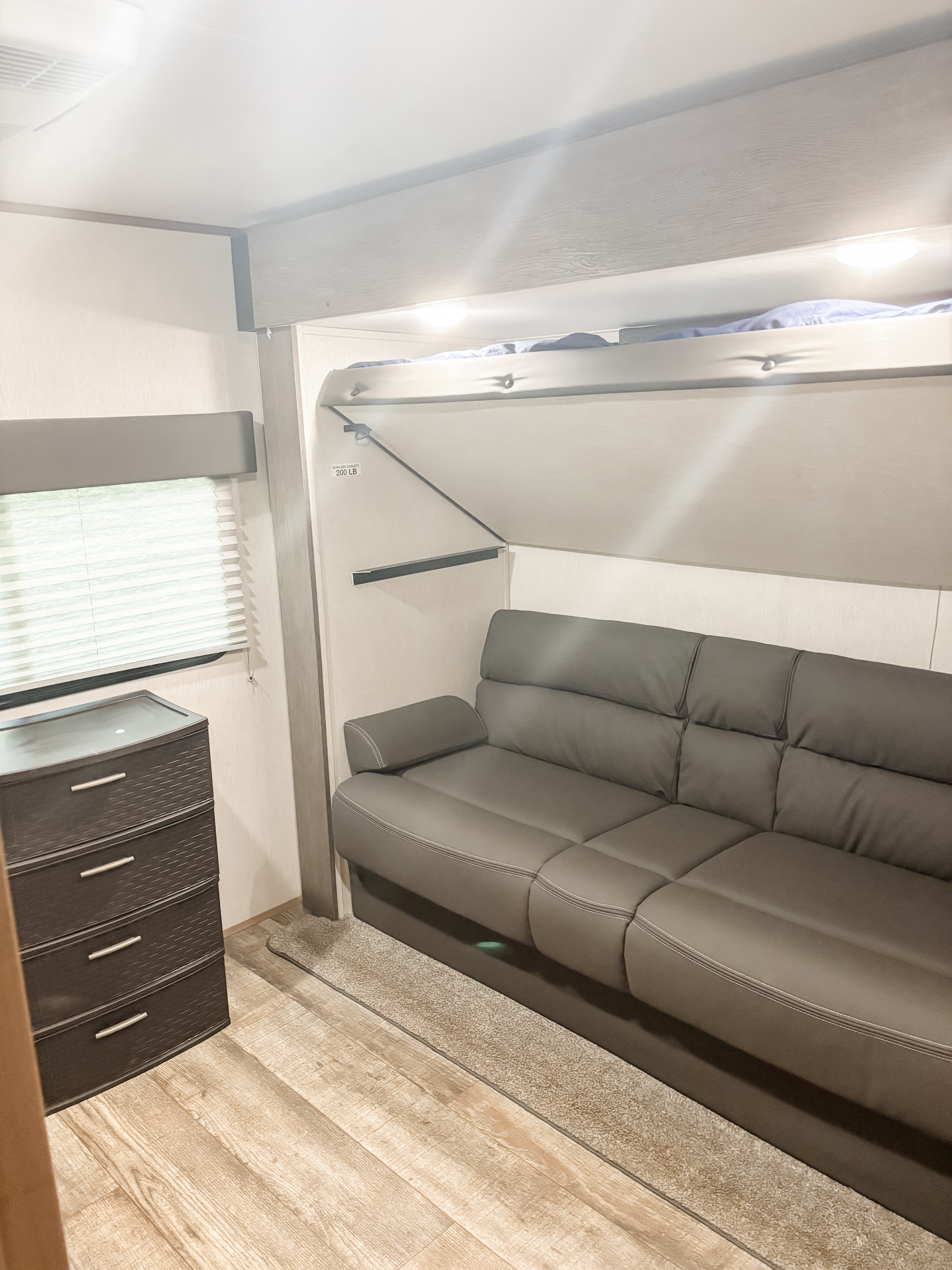 RV rental interior: A cozy space with a gray sofa, fold-up bunk bed (200 lb capacity), dresser, and window blinds.. Forest River 33BH-L 2024