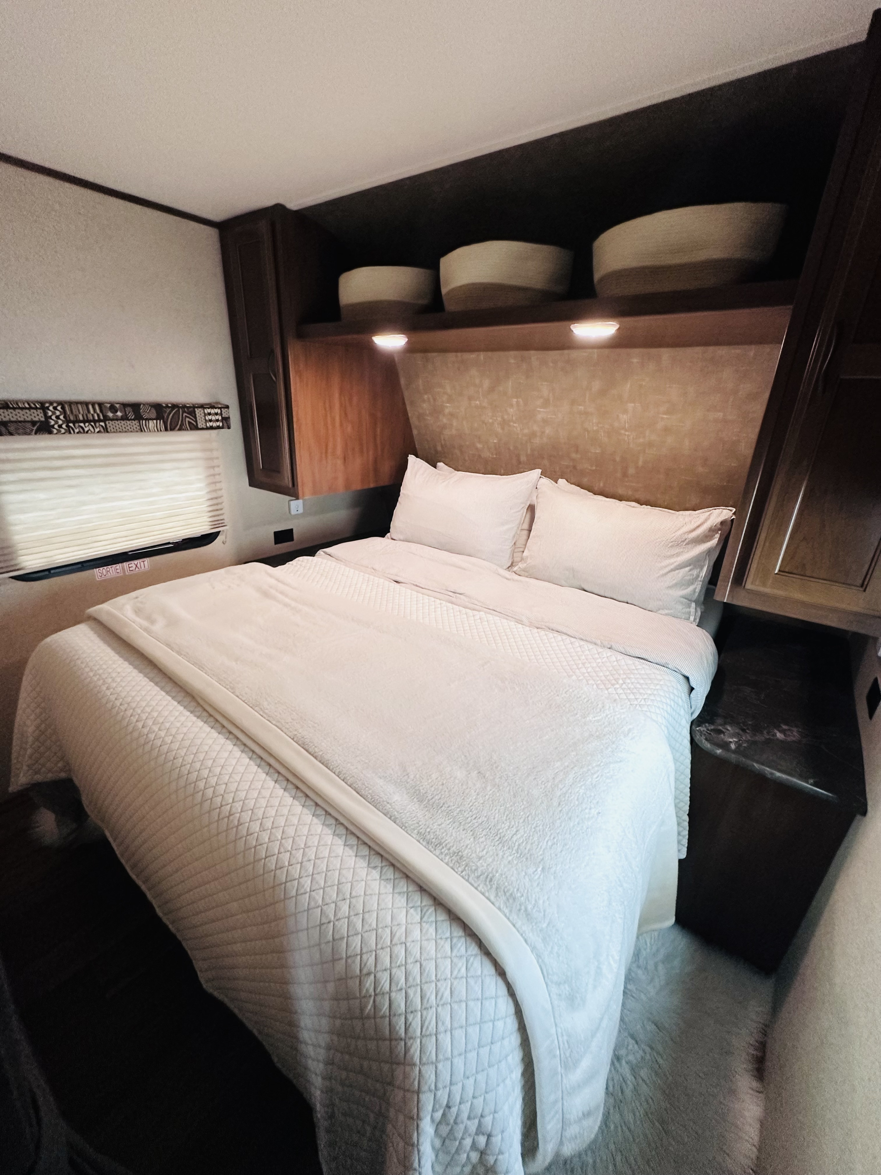 This RV rental bedroom features a comfortable, neatly made bed, overhead storage, and a window with an emergency exit sign.. Jayco Jay Flight 2017