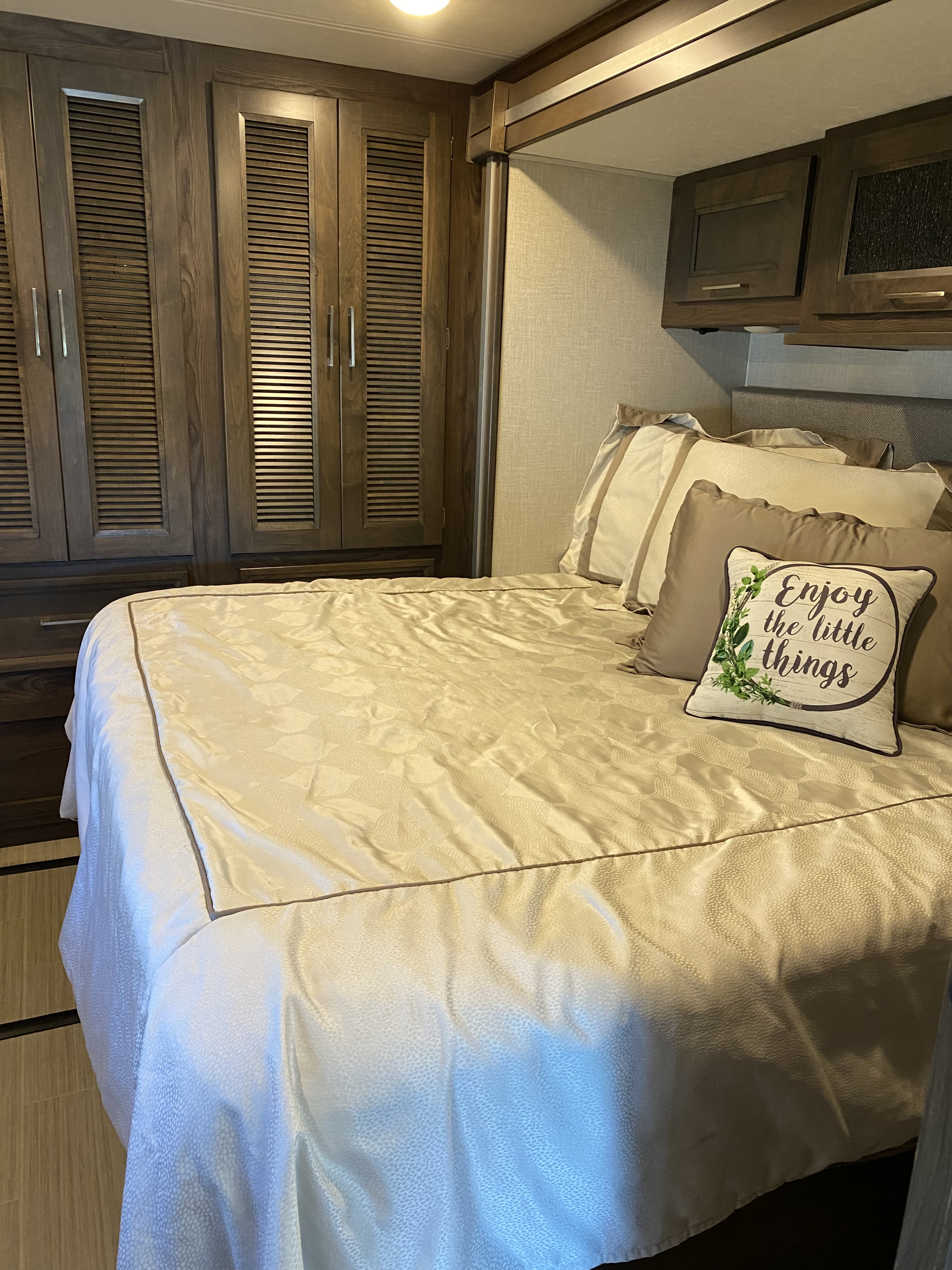Cozy RV rental bedroom with a large, neatly made bed, ample dark wood cabinets, and decorative pillows.. Coachmen Sports Coach 339DS 2019