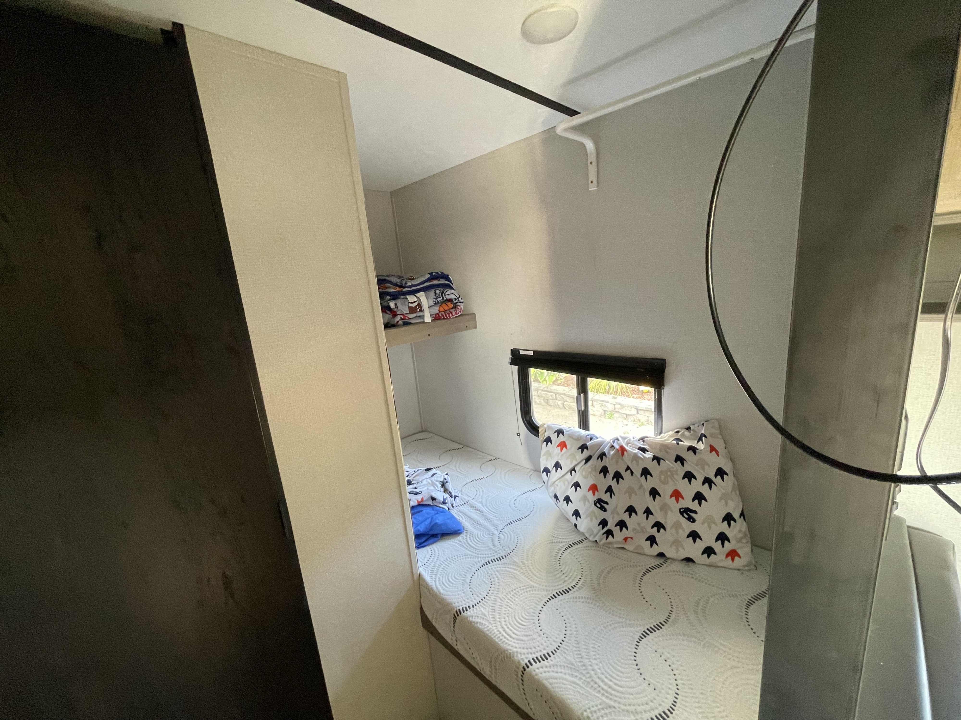 Inside an RV rental: a compact bunk bed with a comfortable mattress, patterned pillow, window, and small shelf.. Keystone RV Hideout 2021