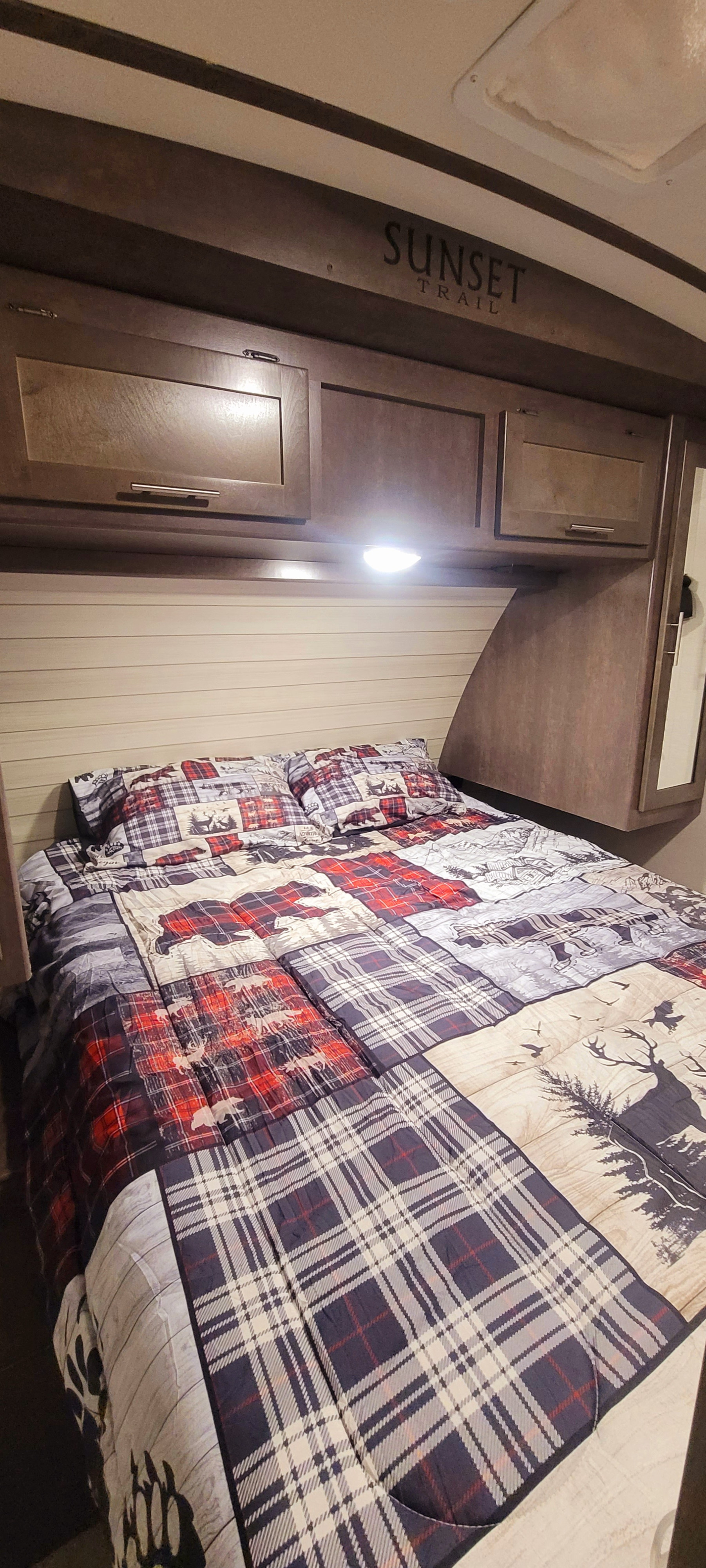 Sunset Trail RV rental bedroom: cozy plaid & nature bedding, overhead storage, and a bright light for comfortable stays.. Crossroads RV Sunset Trail Super Lite 2018