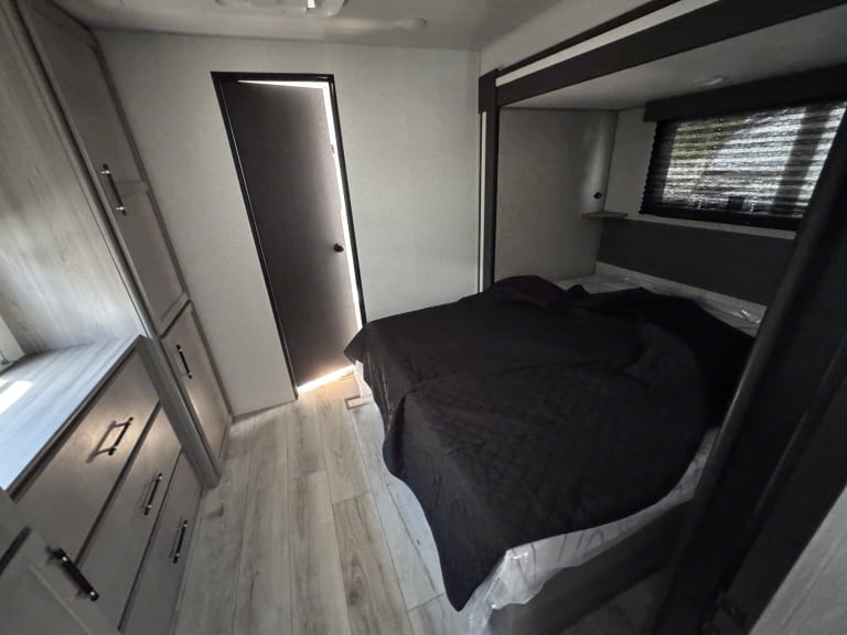 Step into this modern RV rental bedroom, featuring a comfy bed with dark bedding, built-in cabinets, and wood-look flooring.. evergreen sun valley 2015