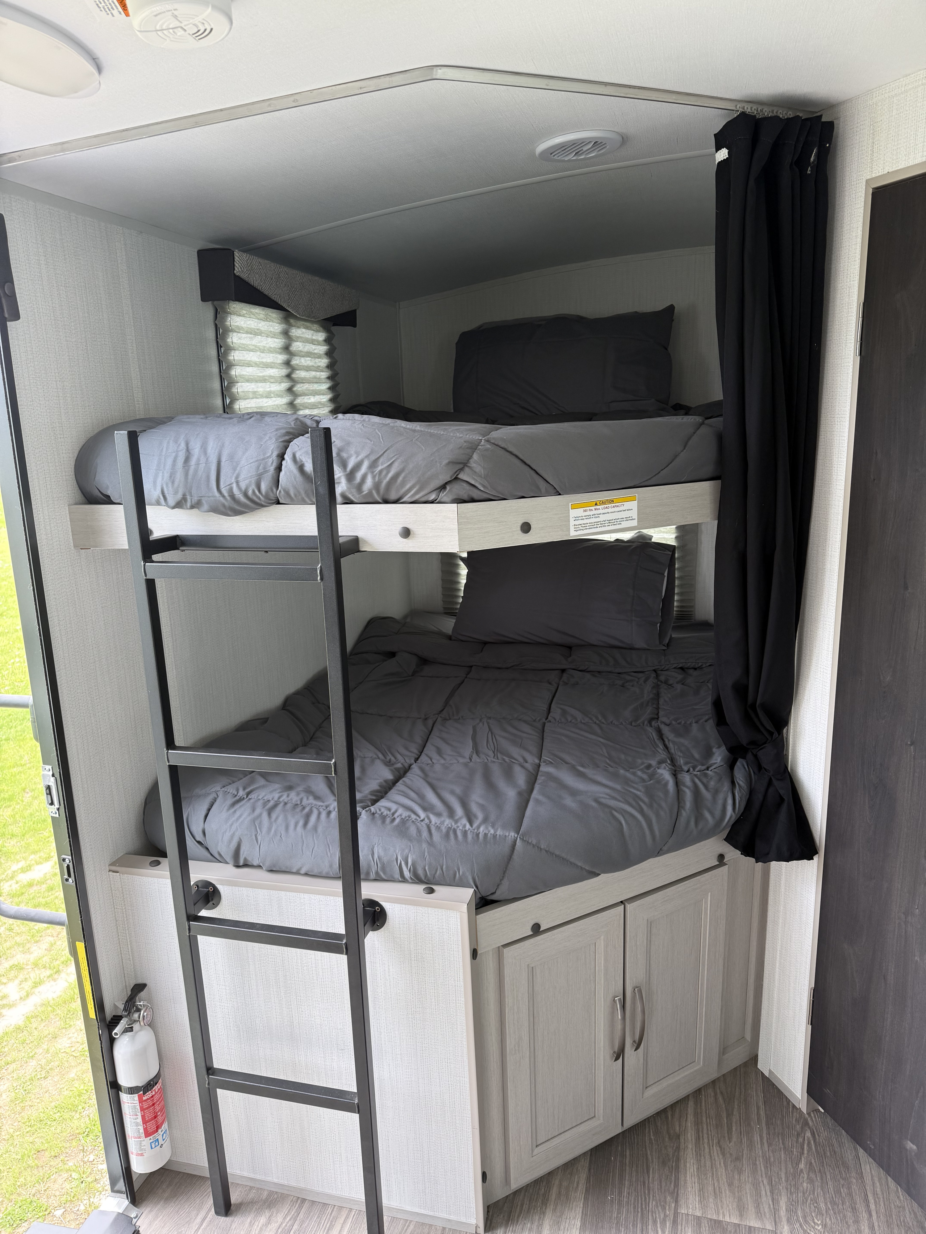 This RV rental features cozy bunk beds with ladder, grey bedding, and privacy curtain, plus a fire extinguisher.. Cruiser RV Shadow Cruiser 2025