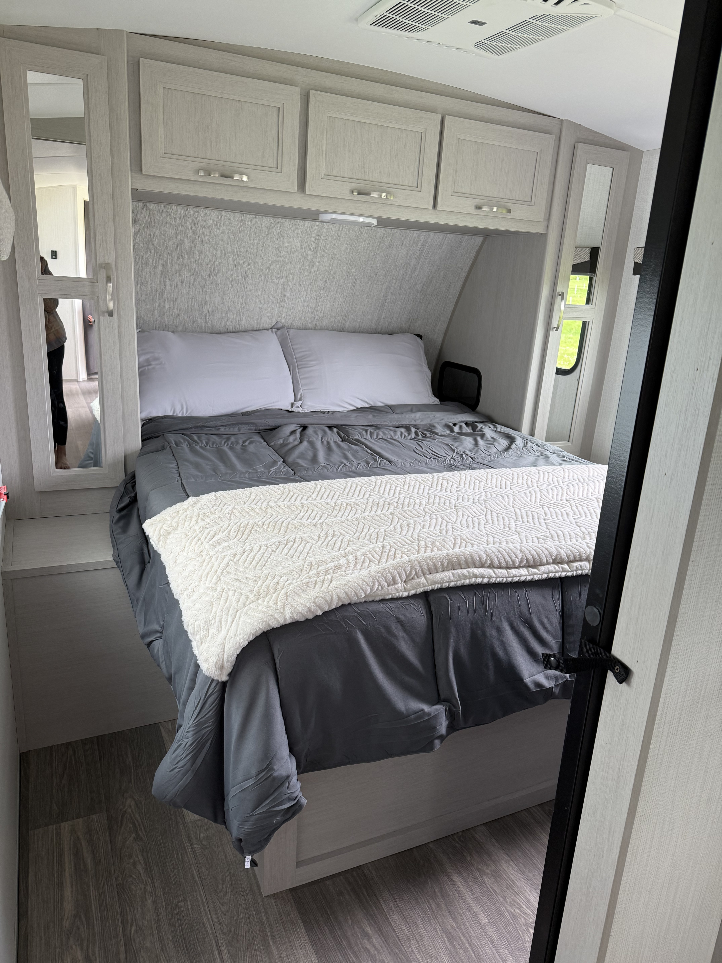 Step into comfort! This modern RV rental bedroom features a cozy bed with gray bedding, overhead cabinets, and a mirrored wardrobe.. Cruiser RV Shadow Cruiser 2025