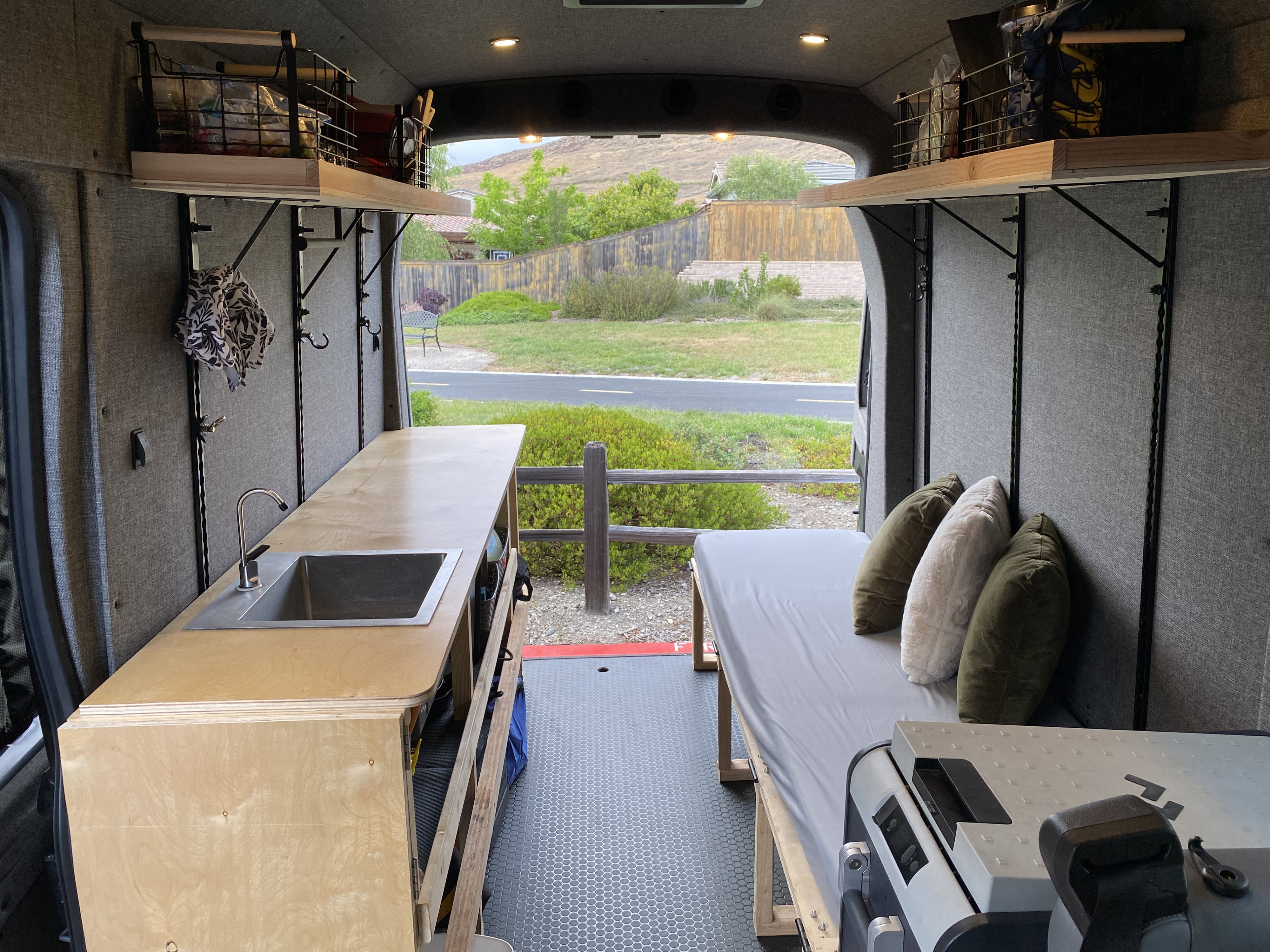 Bright RV rental interior: kitchenette with sink, cozy bed, and organized storage. Scenic outdoor view.. Ford Transit 2016
