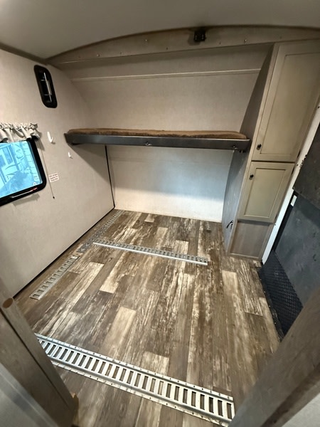RV rental interior of a toy hauler. Features include a raised bunk, floor tracks for cargo tie-downs, and storage cabinets.. Keystone Outback 2020