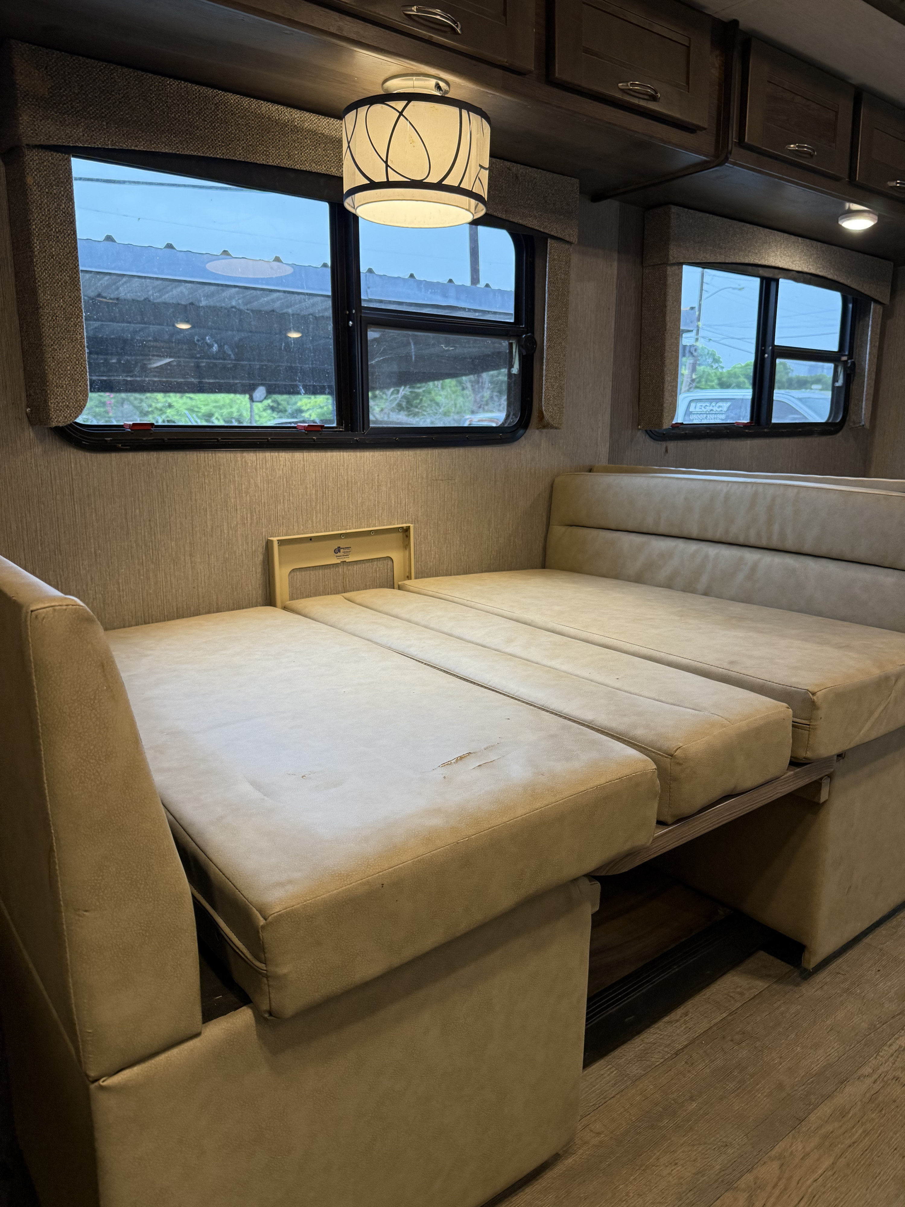 RV rental dinette seating converts to a bed. Light-colored interior with windows, cabinets, and ceiling light. Shows wear.. nexus triumph FORD E450 TRIUMPH 2021