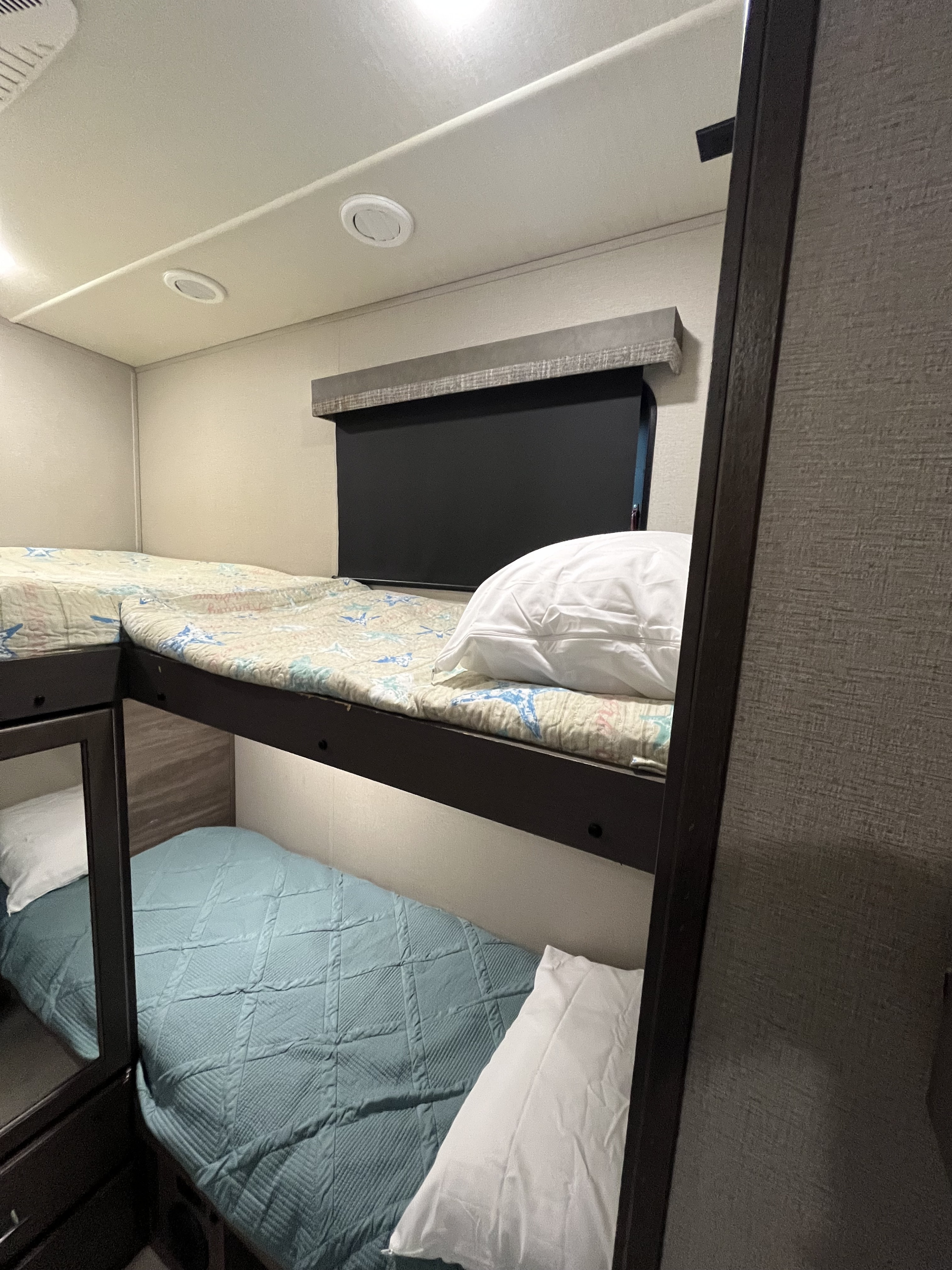 Inside an RV rental: Stacked bunk beds with quilted comforters and pillows provide efficient, cozy sleeping space.. Grand Design Solitude S-Class 2021