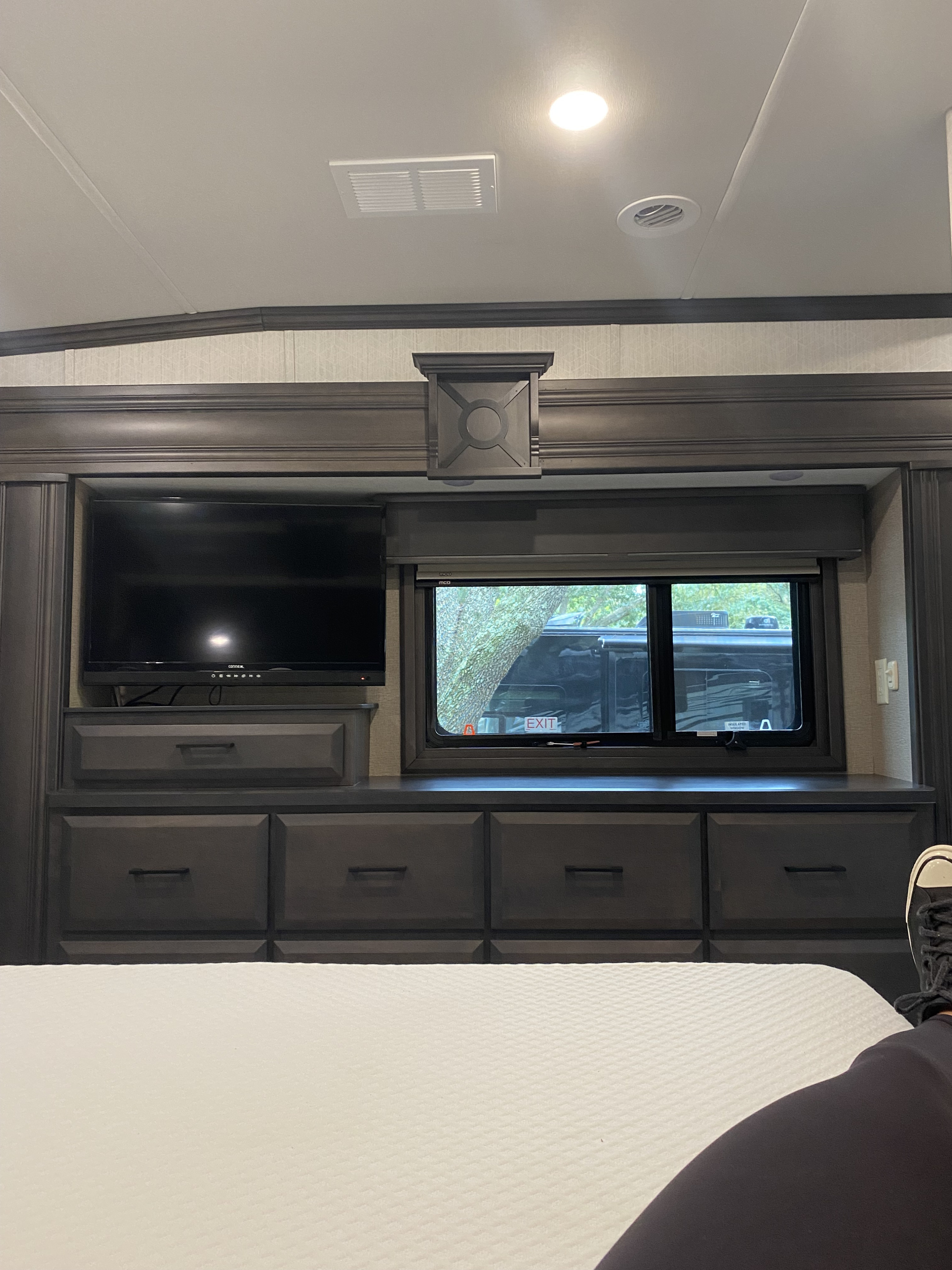 Relaxing RV rental interior: dark wood cabinets, TV, and window view from a comfy bed.. DRV Full House Toy Hauler 2021