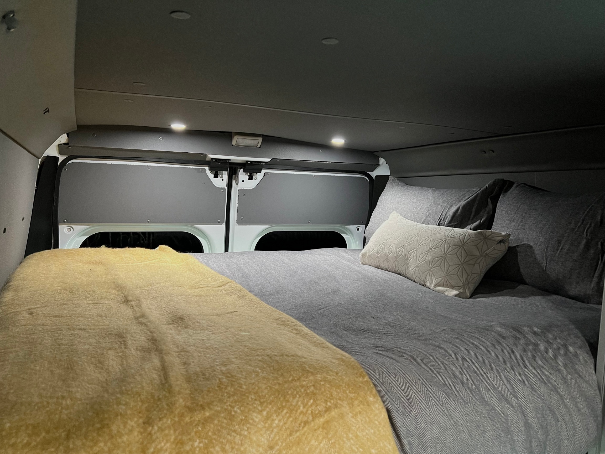 Cozy RV rental bedroom showing a made bed with gray bedding, a yellow blanket, and overhead lighting for comfort.. Dodge Promaster 2500 2020