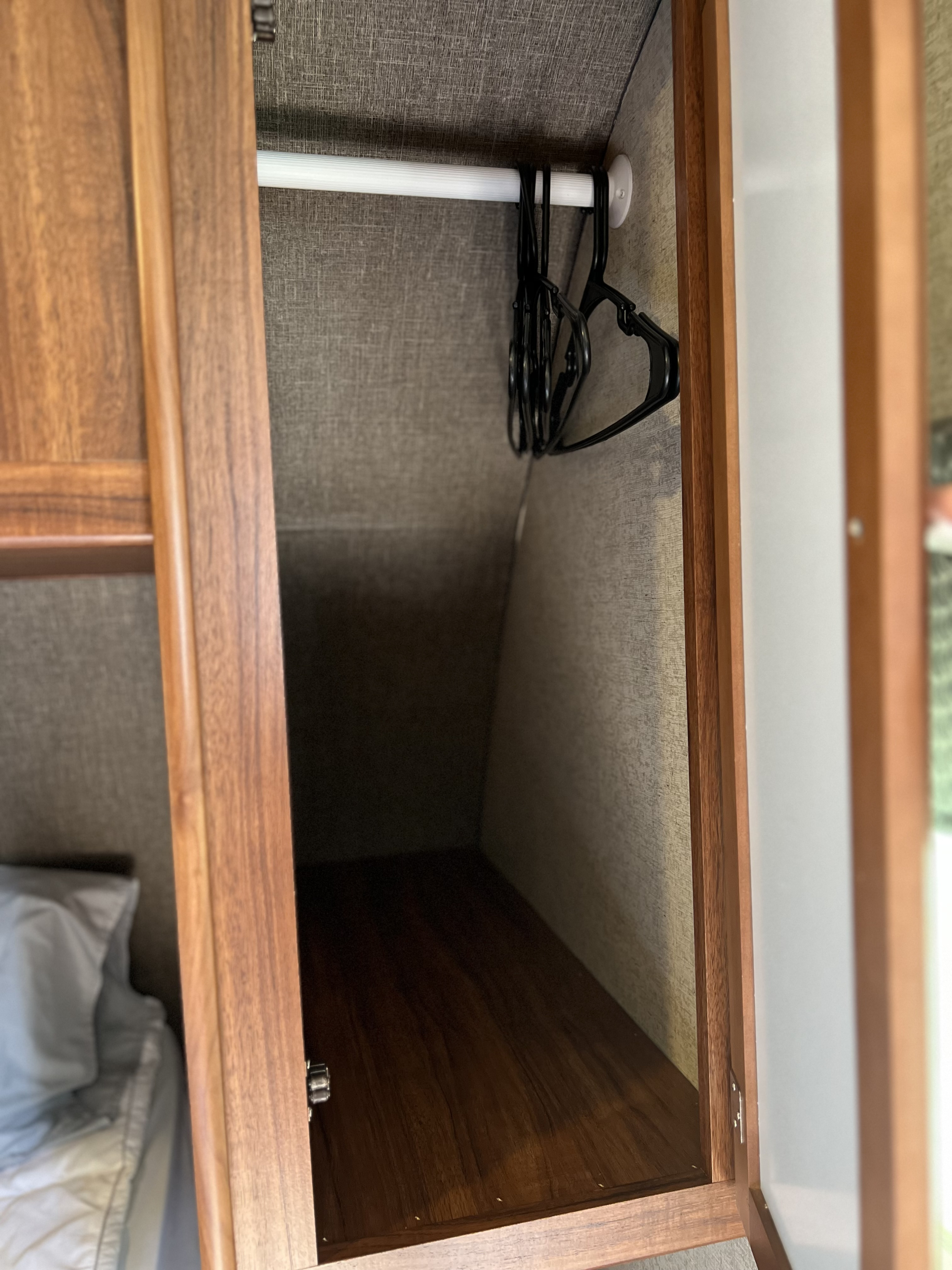 Inside an RV rental: a compact closet with a hanging rod, multiple hangers, and a wooden shelf below for storage.. Heartland RVs Mallard 2018