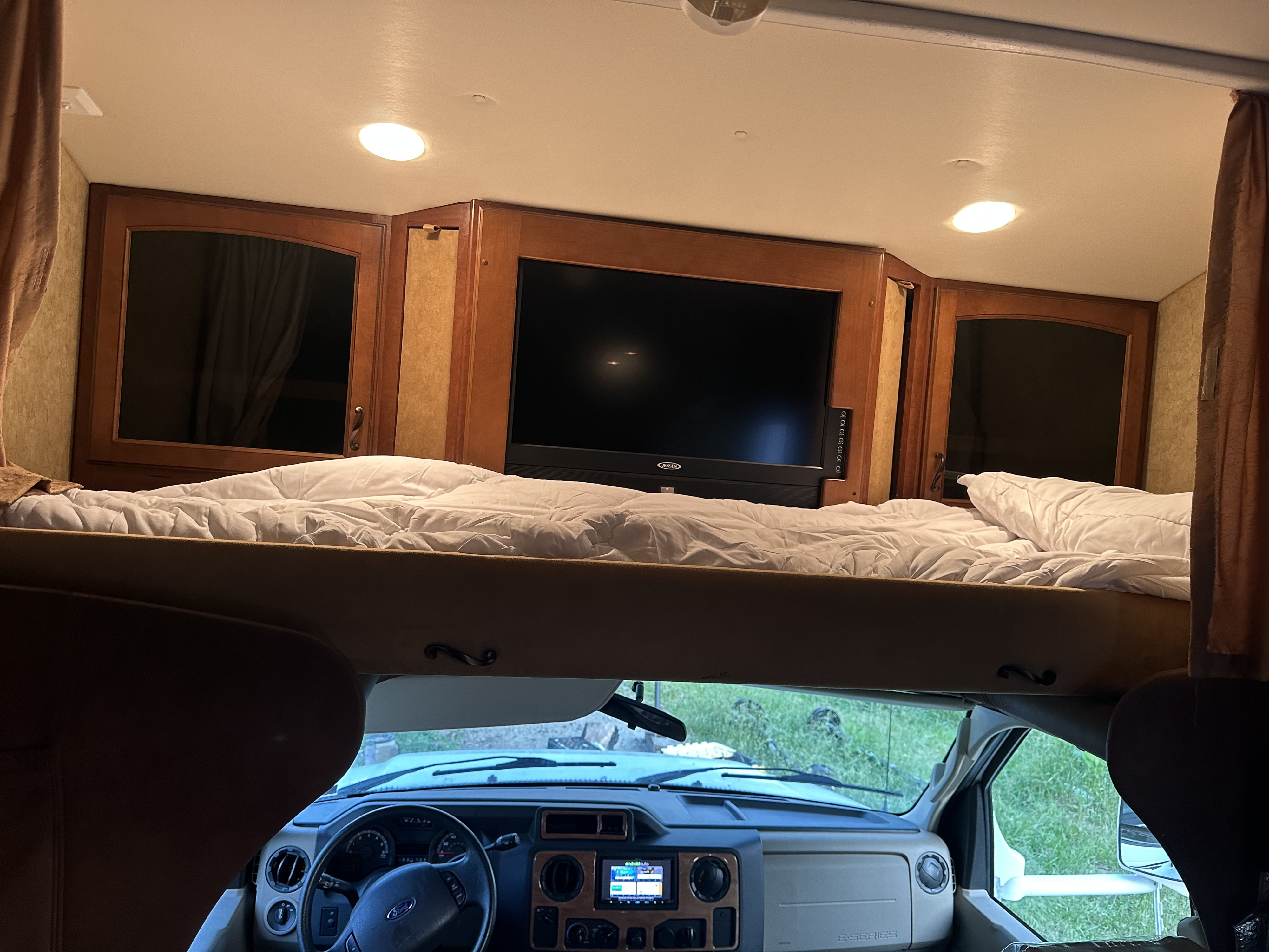 Spacious RV rental interior with an overhead bunk bed, entertainment TV, and the driver's cab.. Jayco Greyhawk 2011