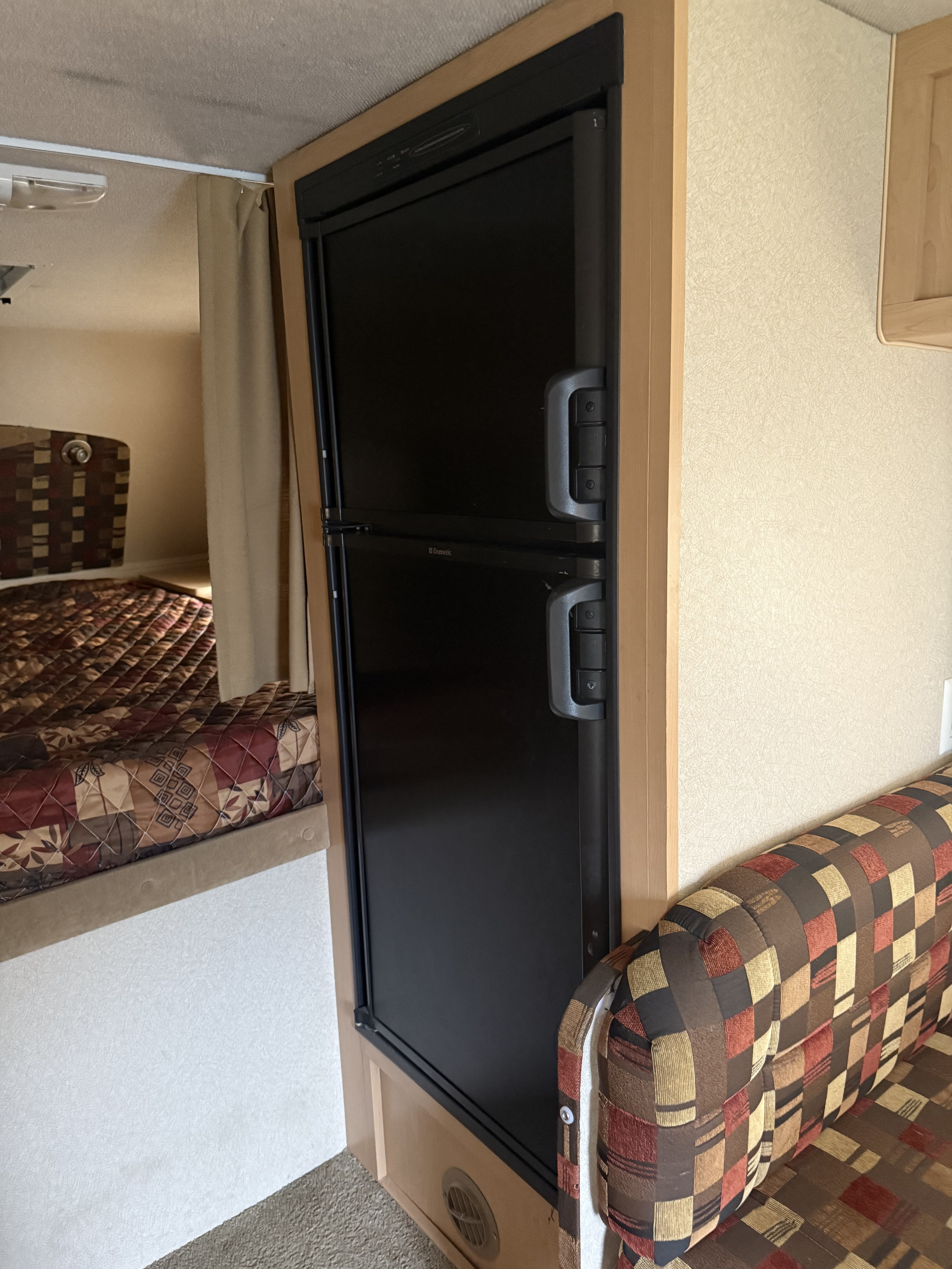RV interior: A Dometic two-door fridge, patterned sofa, and quilted bed show a well-organized rv rental space.. Adventurer Adventurer 2011