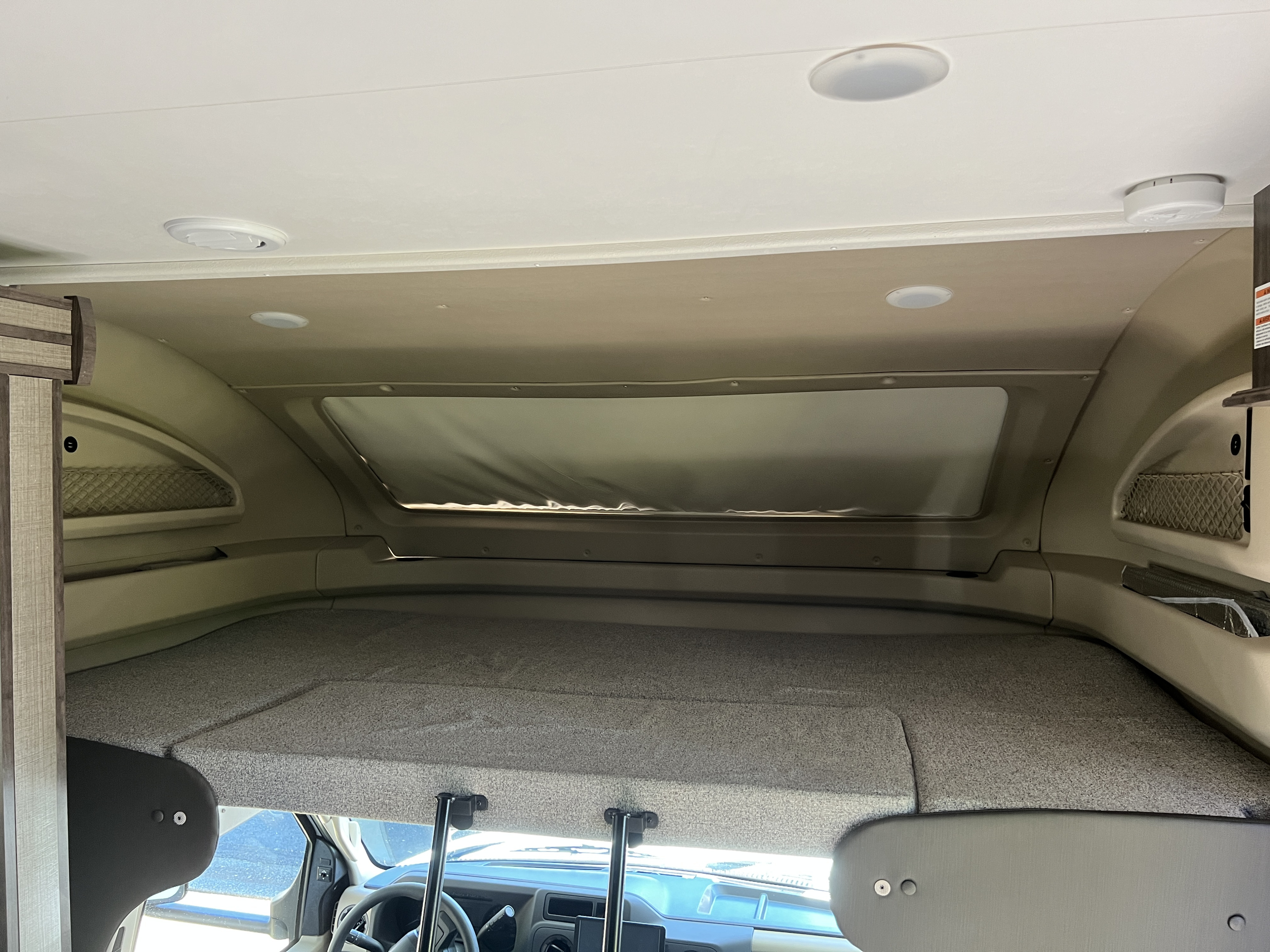 View of a cozy RV rental cabover bunk bed, featuring overhead lights, storage nets, and a front window.. Entegra Coach Odyssey 2022