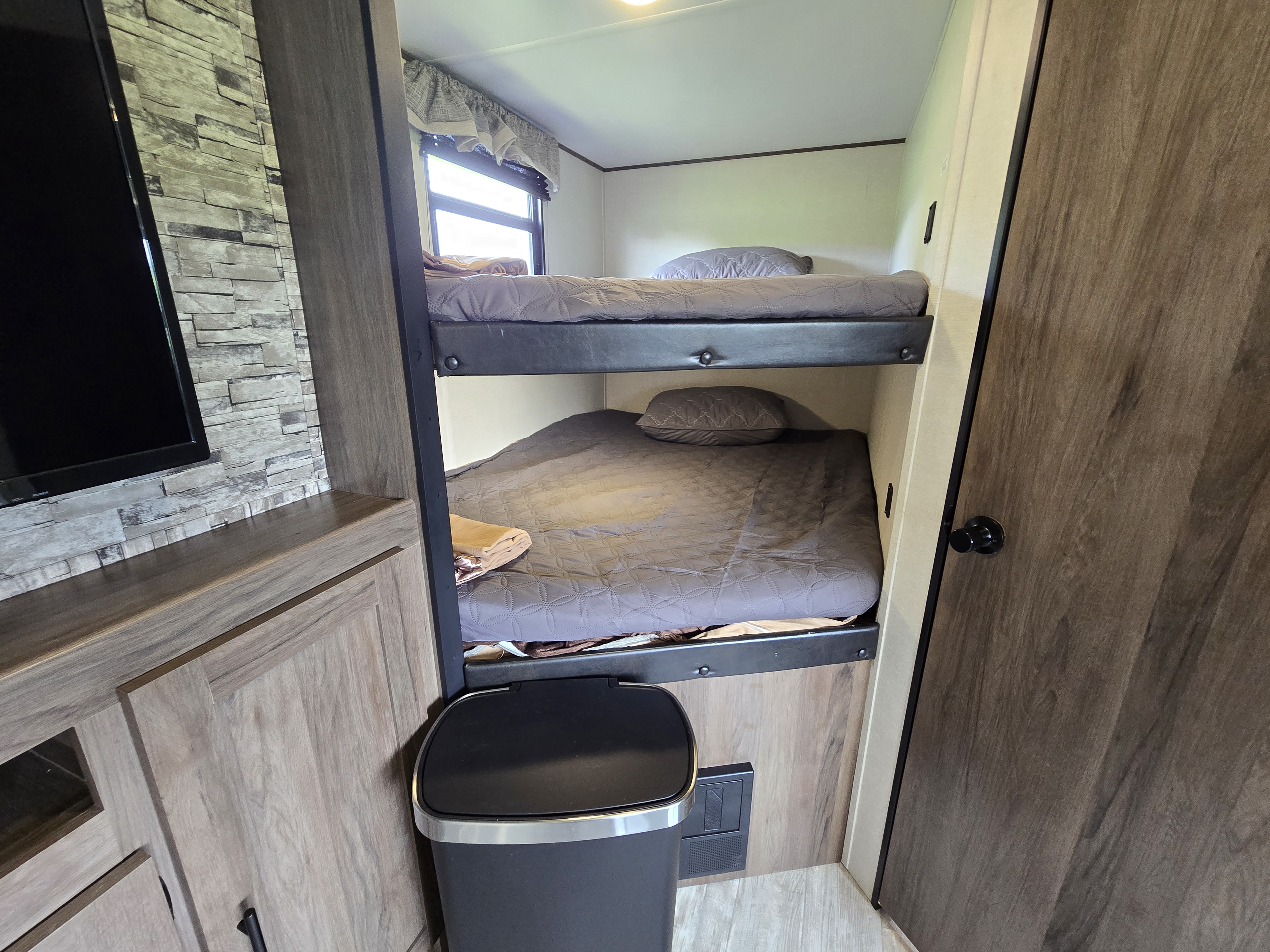 Cozy RV rental interior featuring comfortable bunk beds, a stone accent wall, and wood-look cabinetry.. Avenger Avenger Trailer 2021