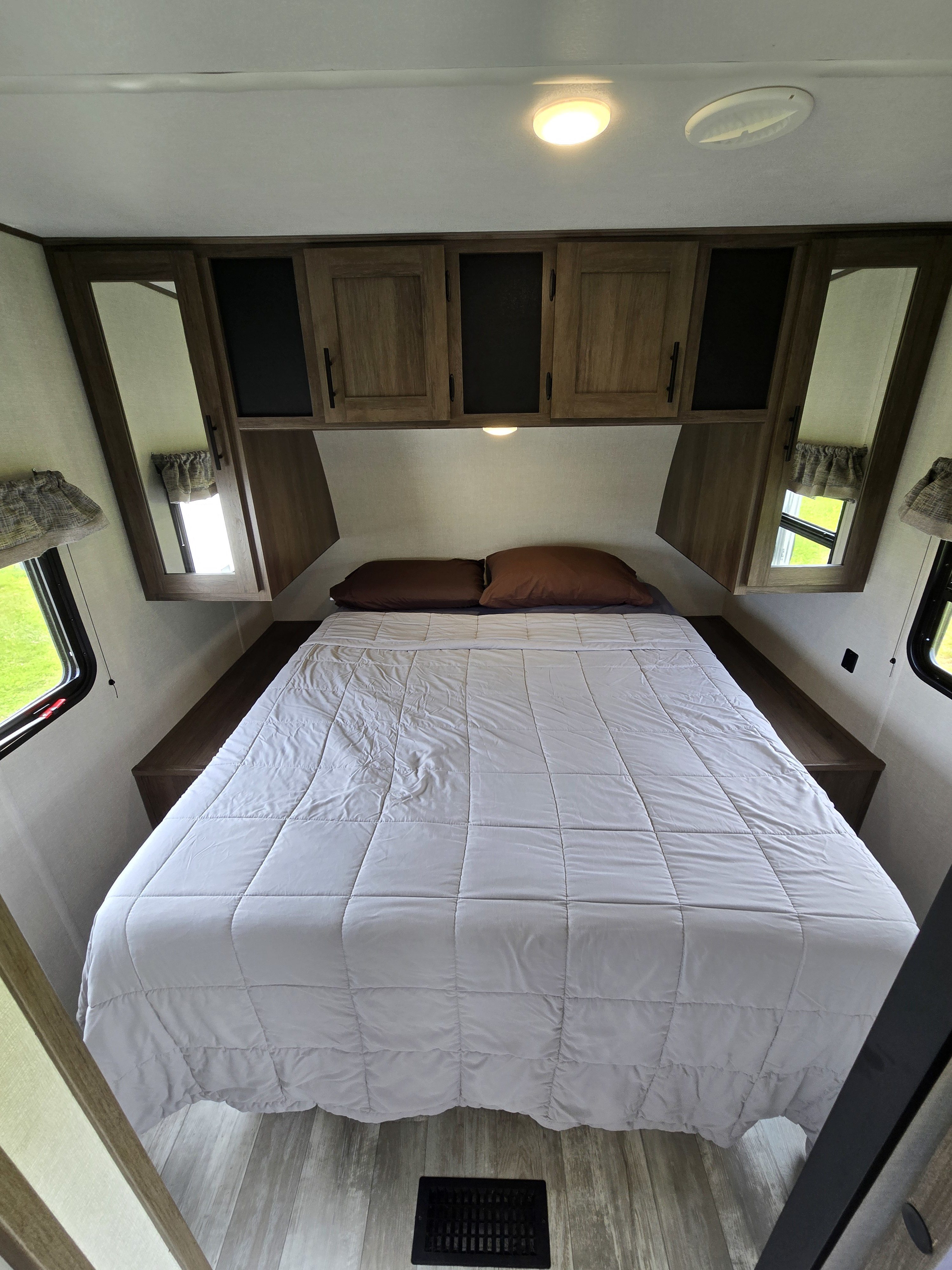 Cozy RV rental bedroom with a neatly made bed, overhead cabinets, and side windows, ready for your adventure.. Avenger Avenger Trailer 2021