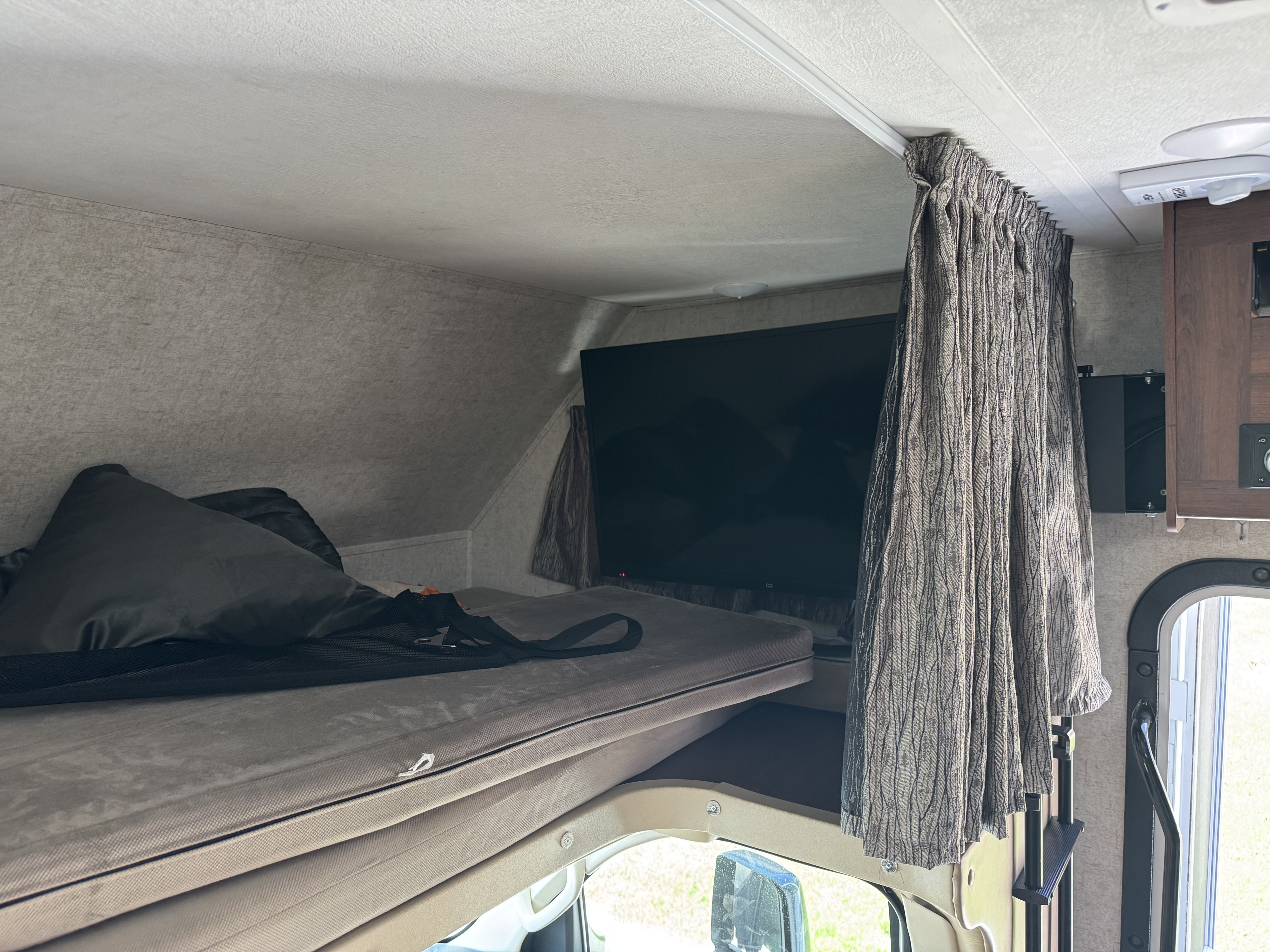Cozy RV rental cab-over bunk with mattress, pillow, and TV, perfect for a comfortable night's sleep on the road.. Forest River Sunseeker 2018