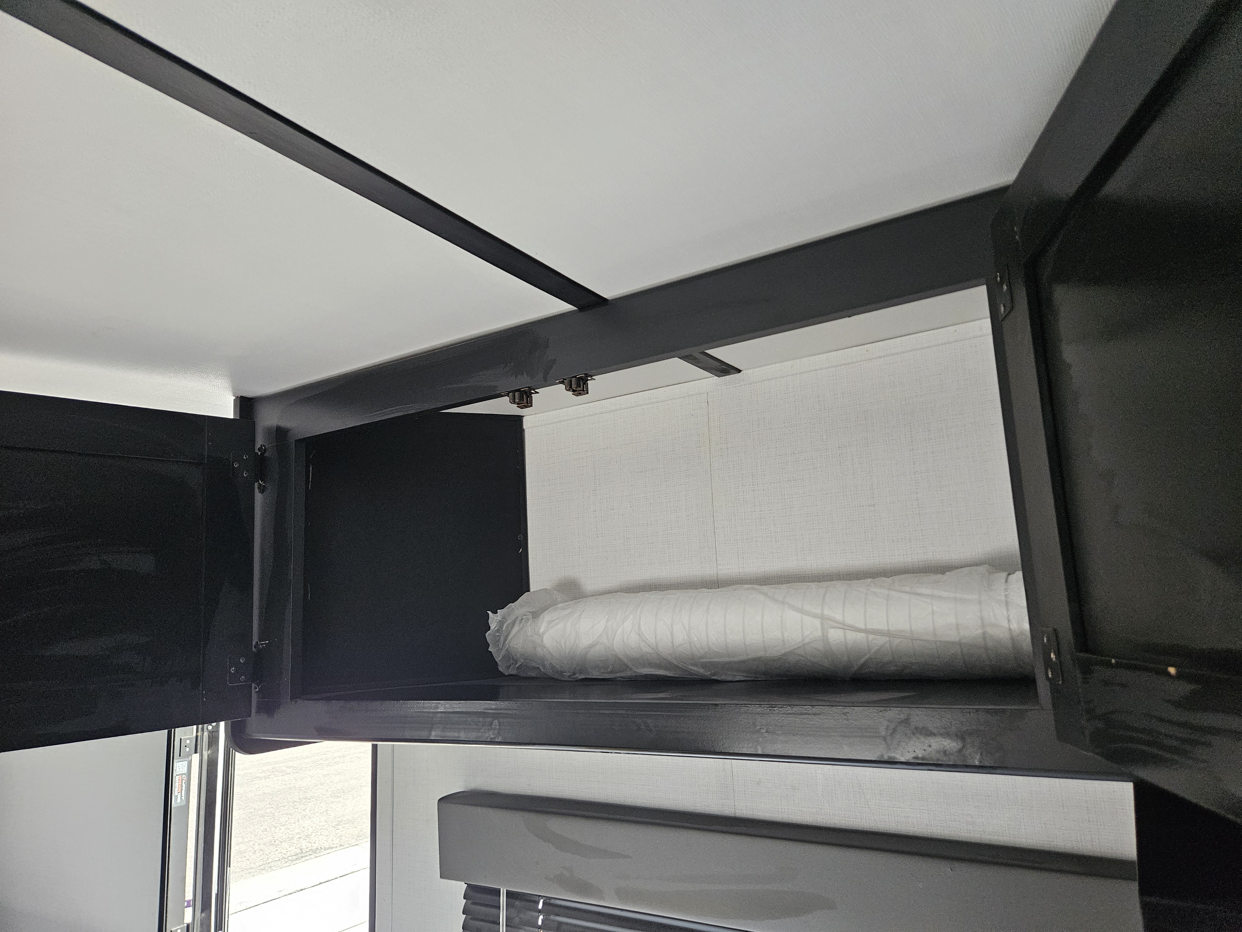 Open overhead cabinet in an RV rental, showing new bedding in plastic. Perfect for storage.. Keystone RV Springdale 2023