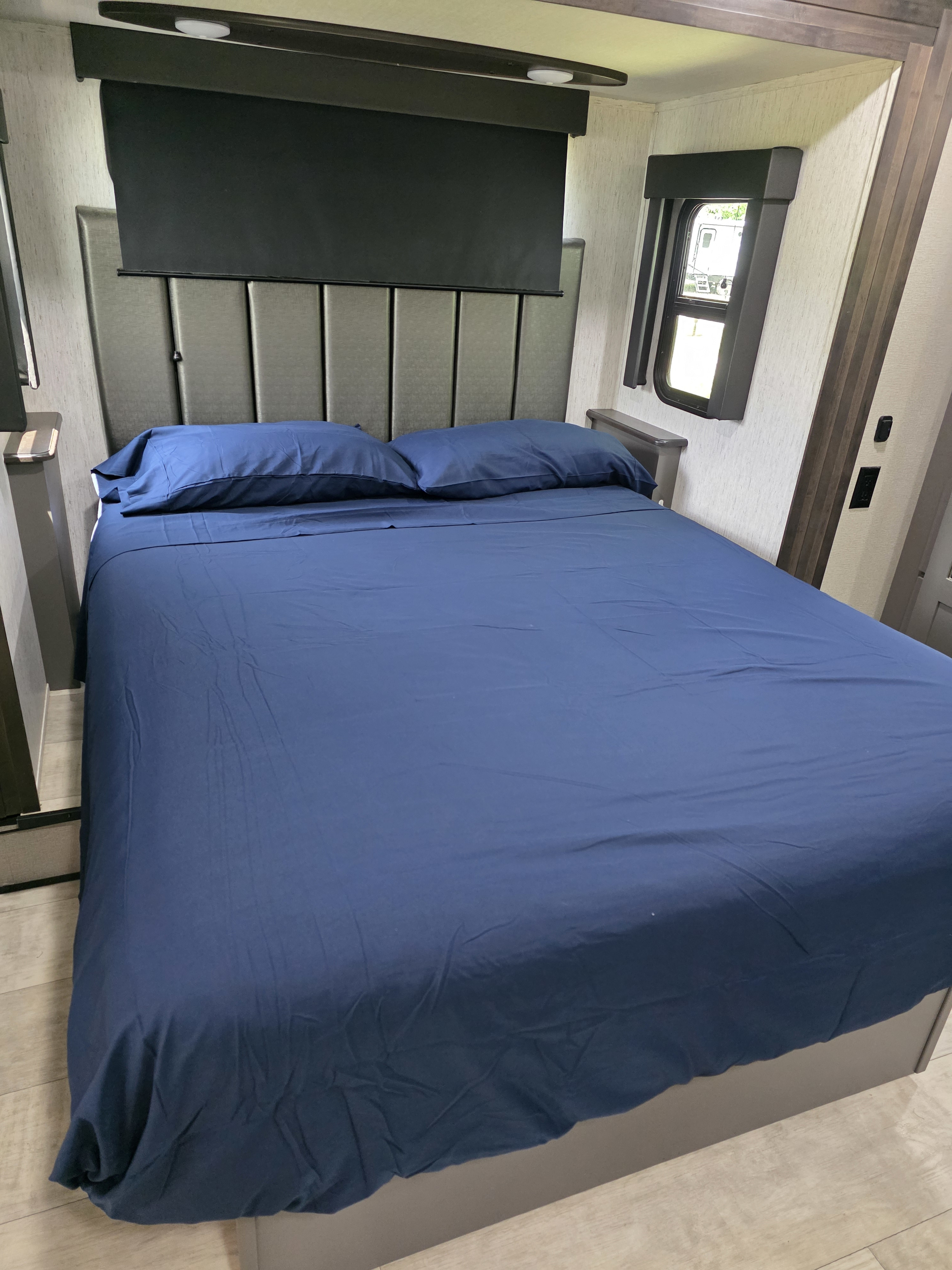 Comfortable RV rental bedroom with a bed featuring blue sheets, headboard, and window. Perfect for your next adventure.. Grand Design Momentum 2022