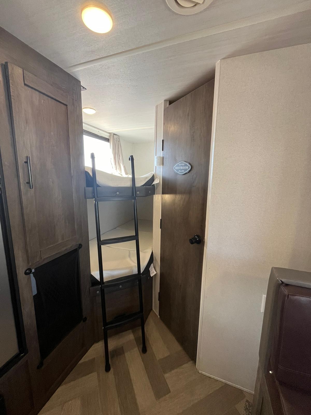 Inside an RV rental: Looking toward the back, you see bunk beds with a ladder on the left, and a restroom door on the right.. Forest River EVO 2021