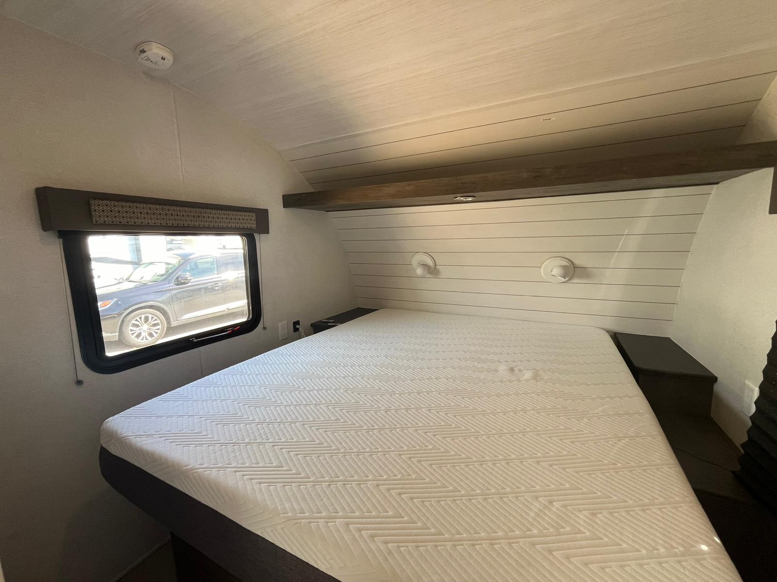 Comfortable RV rental bedroom featuring a large bed with a patterned mattress, shiplap headboard, and wall lights.. Forest River EVO 2021