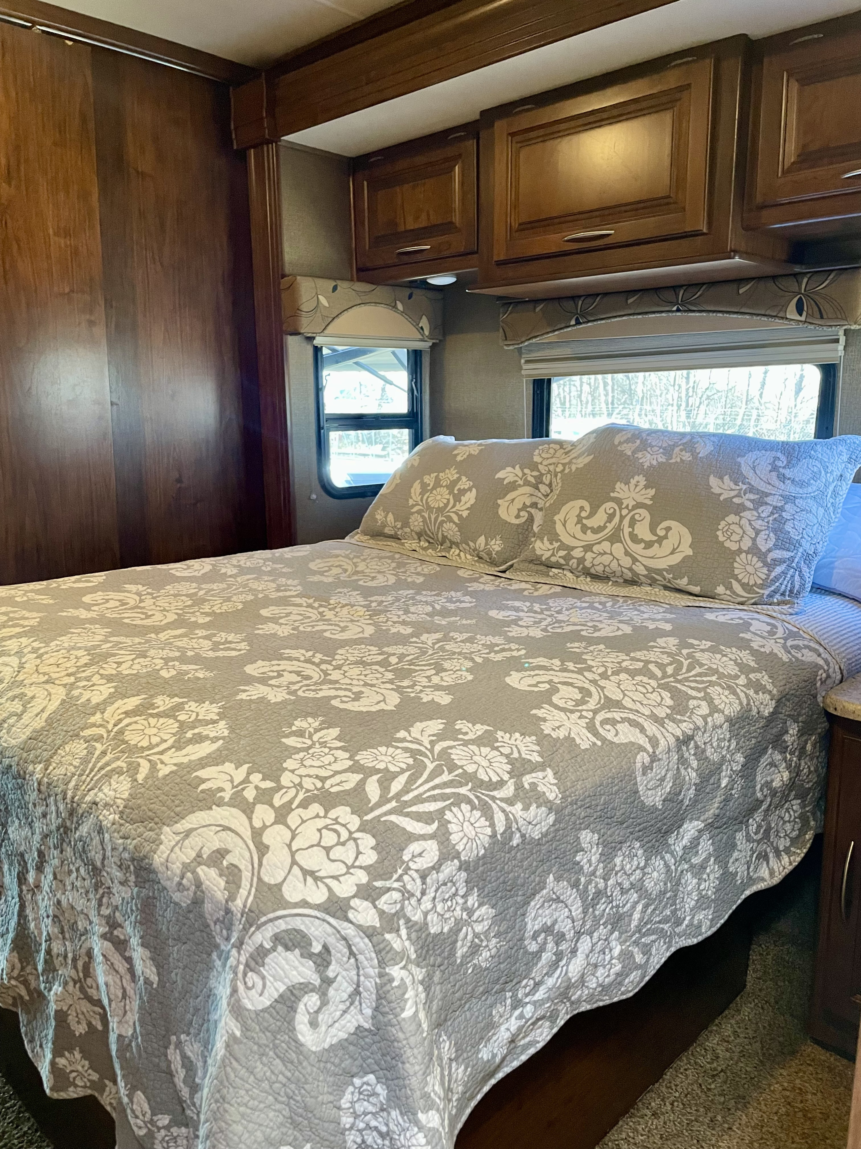 Step into comfort: This RV rental bedroom features a cozy bed with floral bedding, wood cabinets, and scenic windows.. Coachmen Mirada 2016