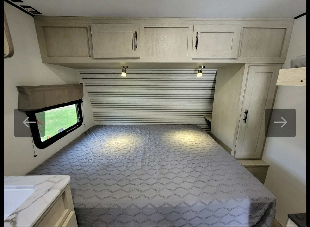 Cozy RV rental bedroom with a large bed, striped headboard, overhead cabinets, and a scenic window.. Forest River 16BH 2024