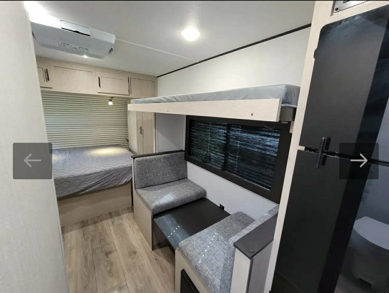 RV rental interior with bedroom, overhead cabinets, bunk beds over a dinette, and a refrigerator.. Forest River 16BH 2024