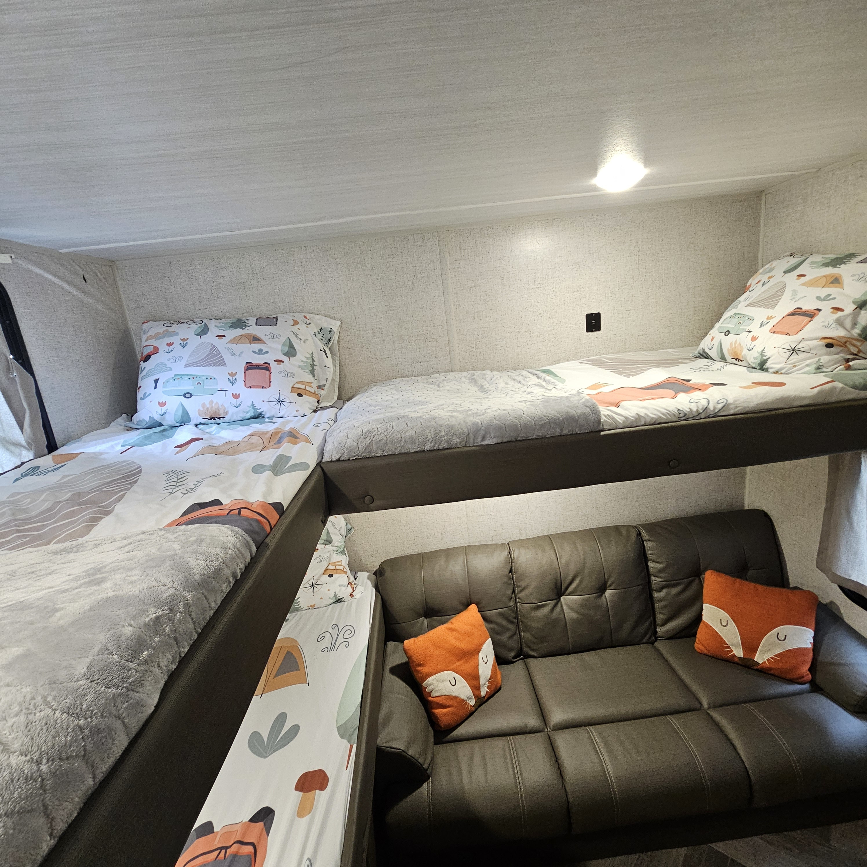 Inside an RV rental: a cozy bunk bed area with fun camping-themed bedding, plus a comfy couch below.. Forest River Salem Cruise Lite 2021