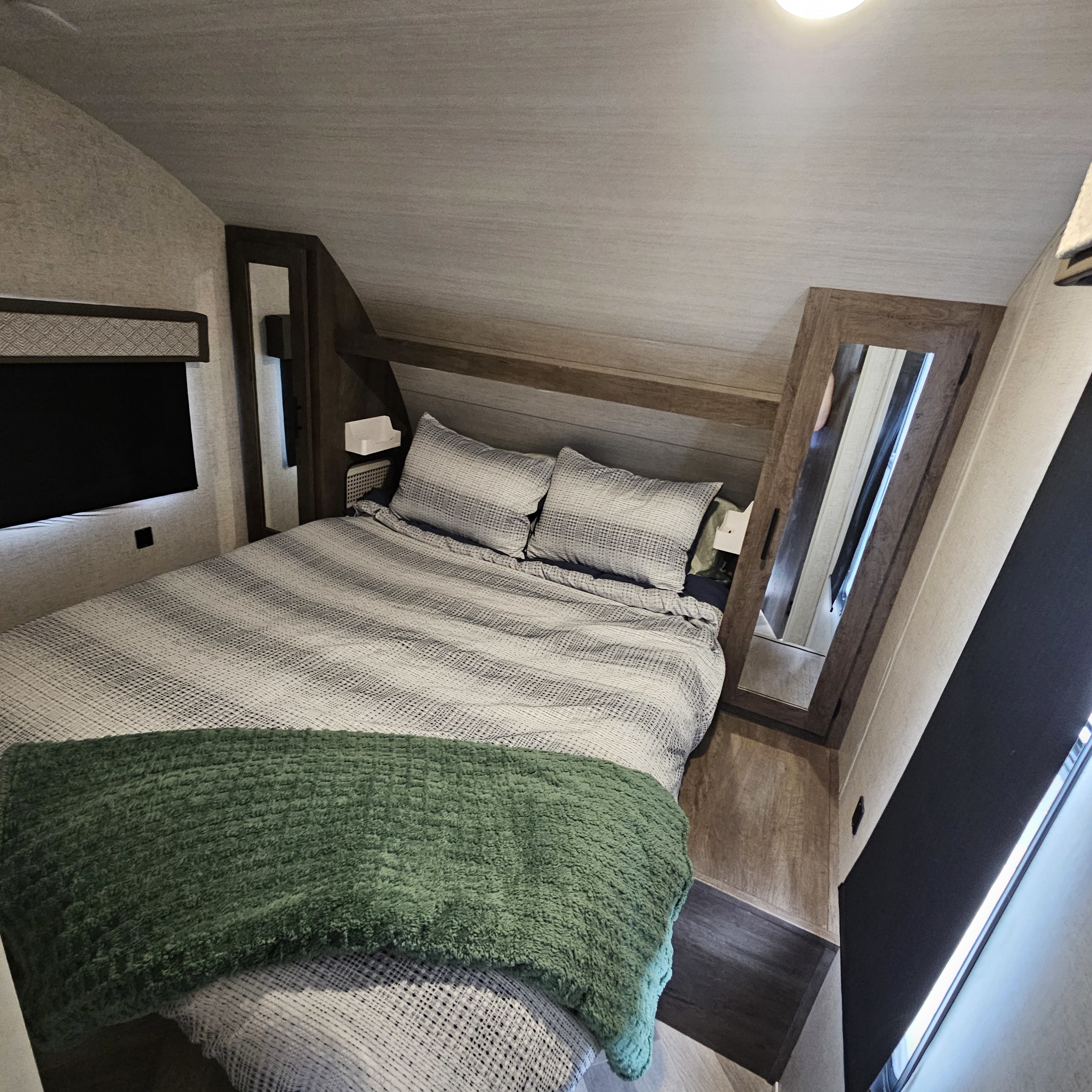 RV rental bedroom interior: striped bed with green blanket, built-in TV, and standing mirror.. Forest River Salem Cruise Lite 2021