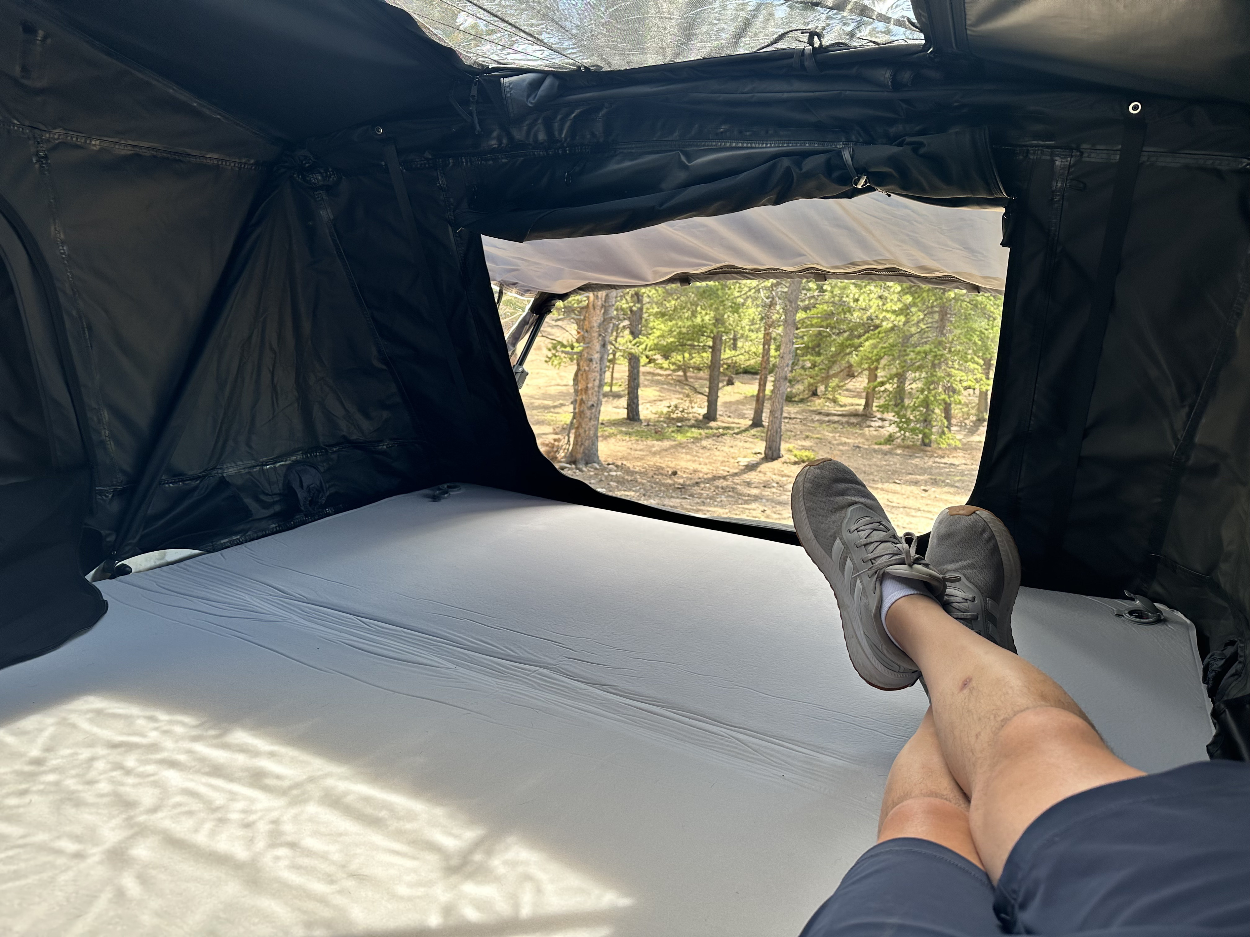 Relaxing inside a rooftop tent from an RV rental, enjoying the sunny forest view. Ideal for your next camping adventure.. 3TMCZ5AN8MM421865 Toyota 2021