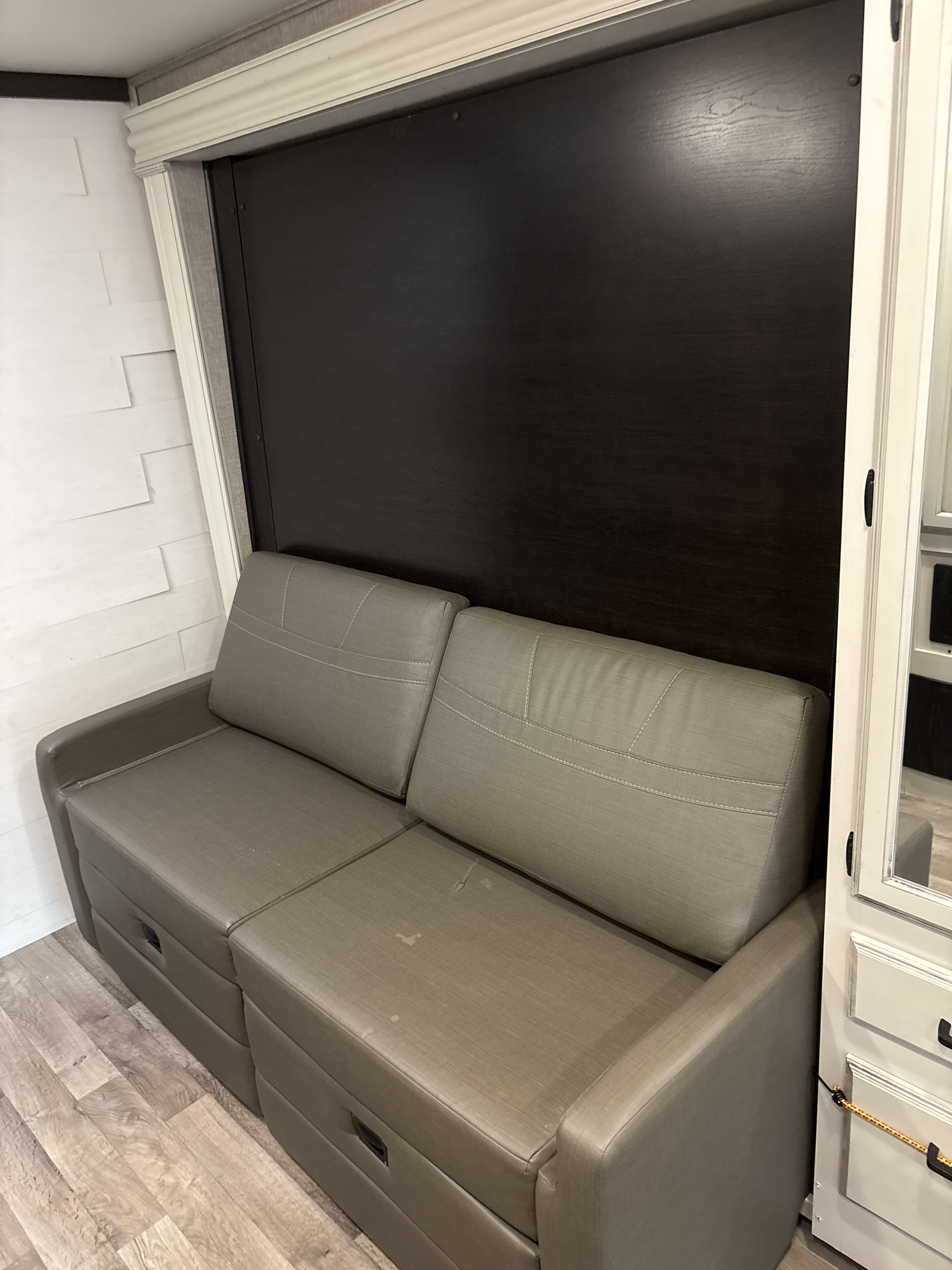 Inside an RV rental: a modern grey pull-out sofa bed with dark wood accent wall and light wood flooring.. Jayco Redhawk 2022