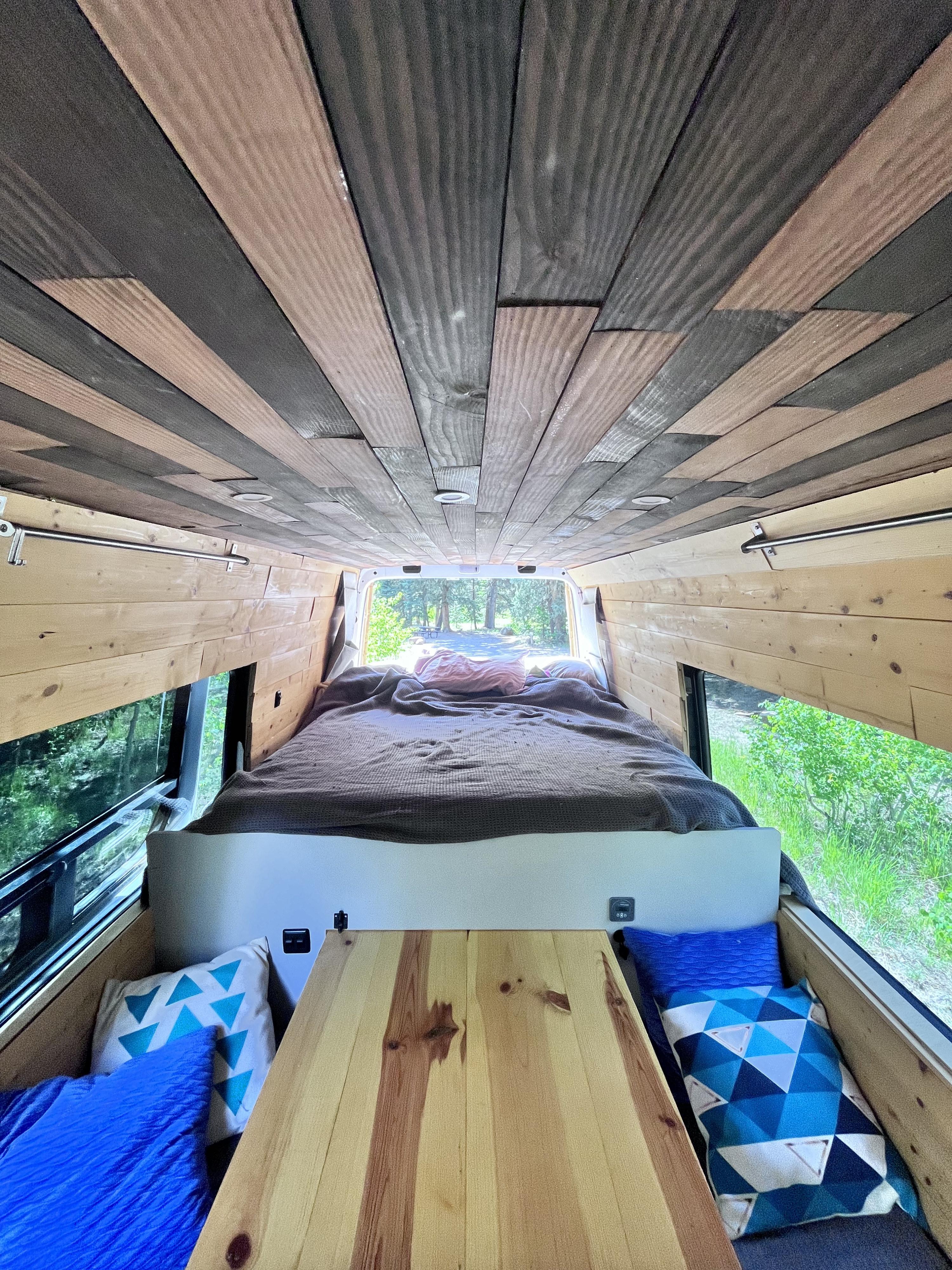 Inside a unique RV rental: custom wooden ceiling & walls, cozy bed with outdoor views. Ideal for van life travel.. Mercedes-Benz Sprinter 2011