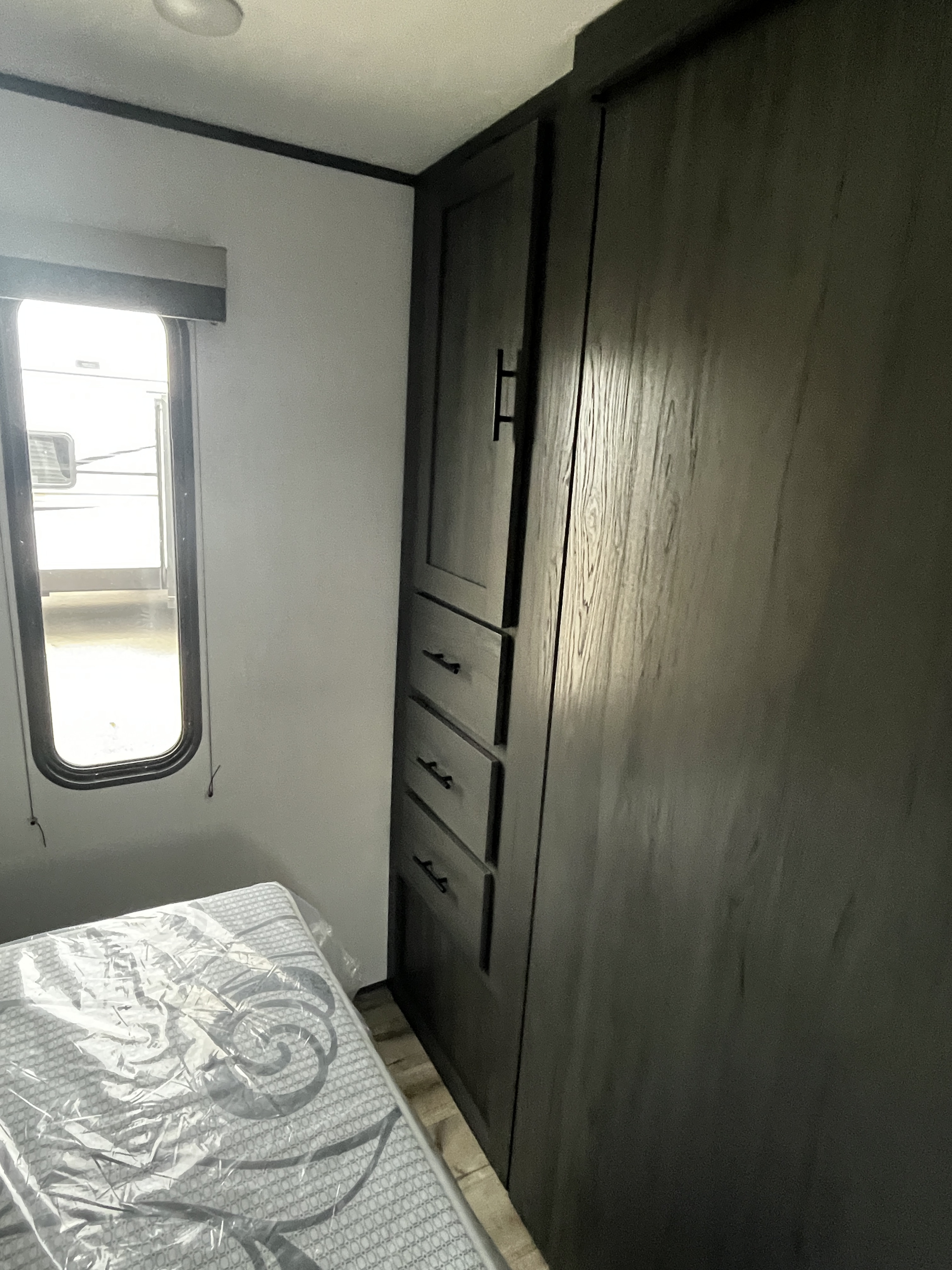 RV rental interior: A compact bedroom with a bed, window, and dark wood-look storage cabinets, ready for your adventure.. Dutchmen Aspen Trail 2025